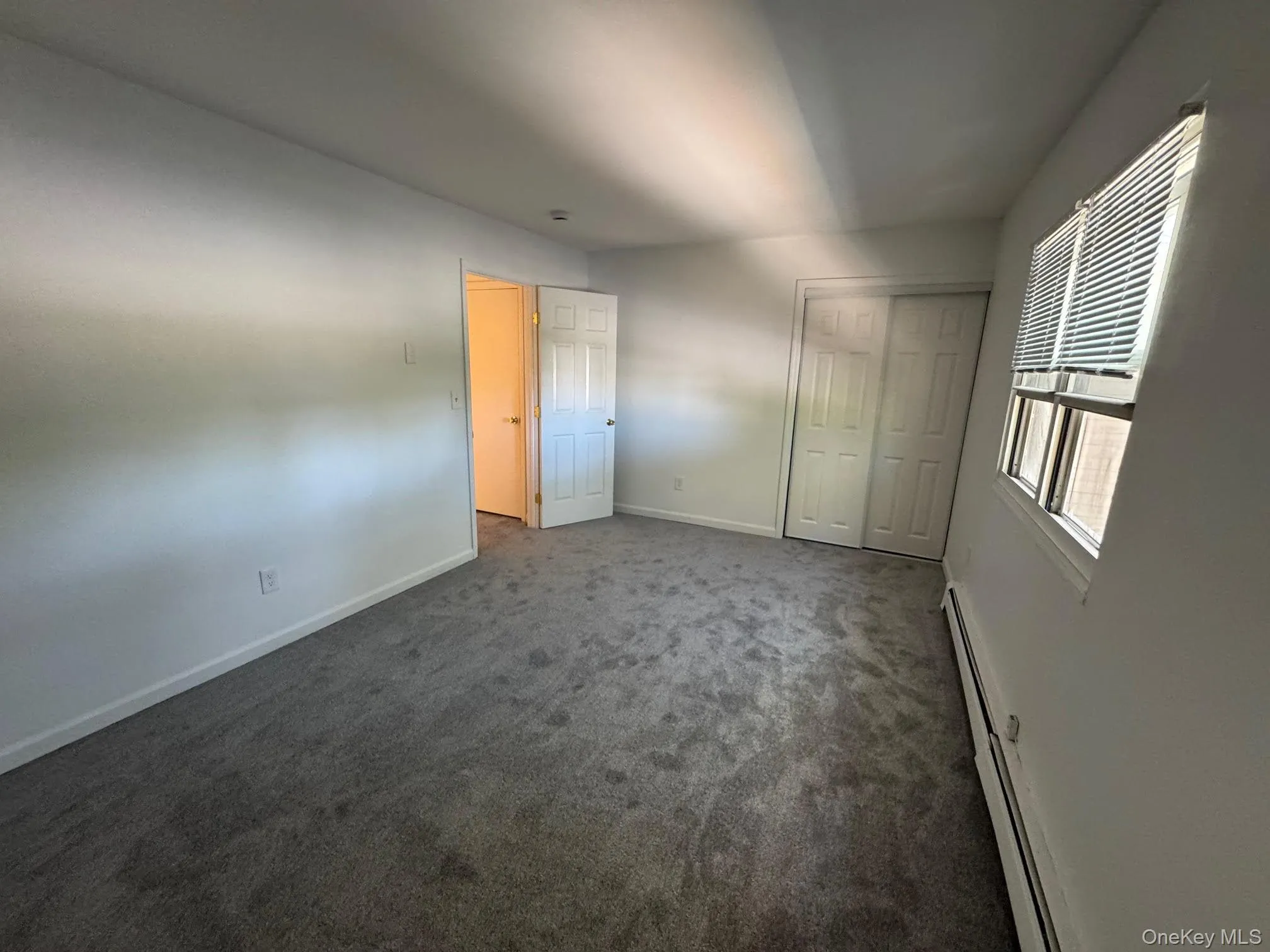 Unfurnished bedroom featuring a baseboard heating unit, dark colored carpet, and a closet Unfurnished bedroom featuring a baseboard heating unit, dark colored carpet, and a closet