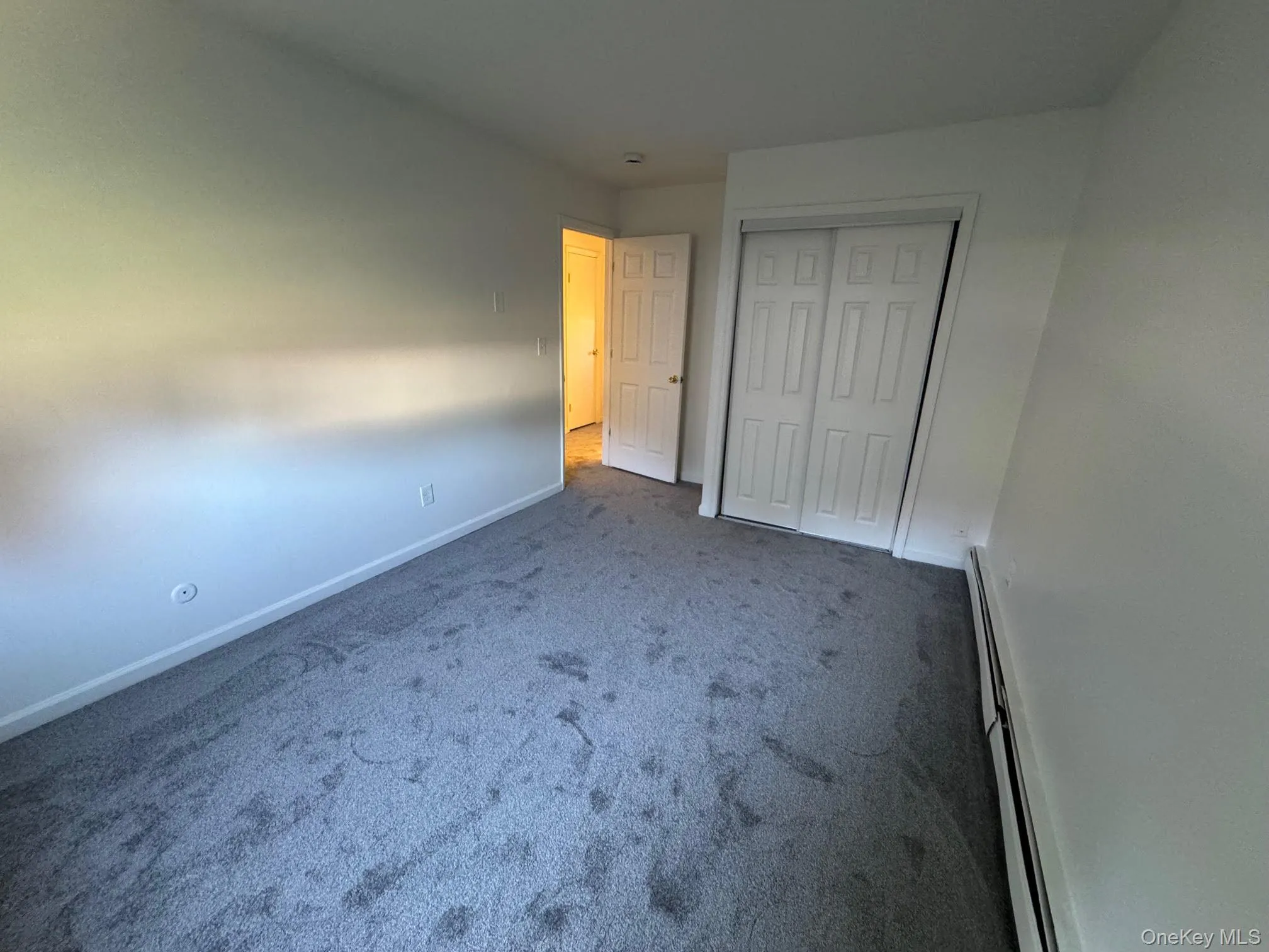 Unfurnished bedroom with baseboard heating, carpet floors, and a closet Unfurnished bedroom with baseboard heating, carpet floors, and a closet
