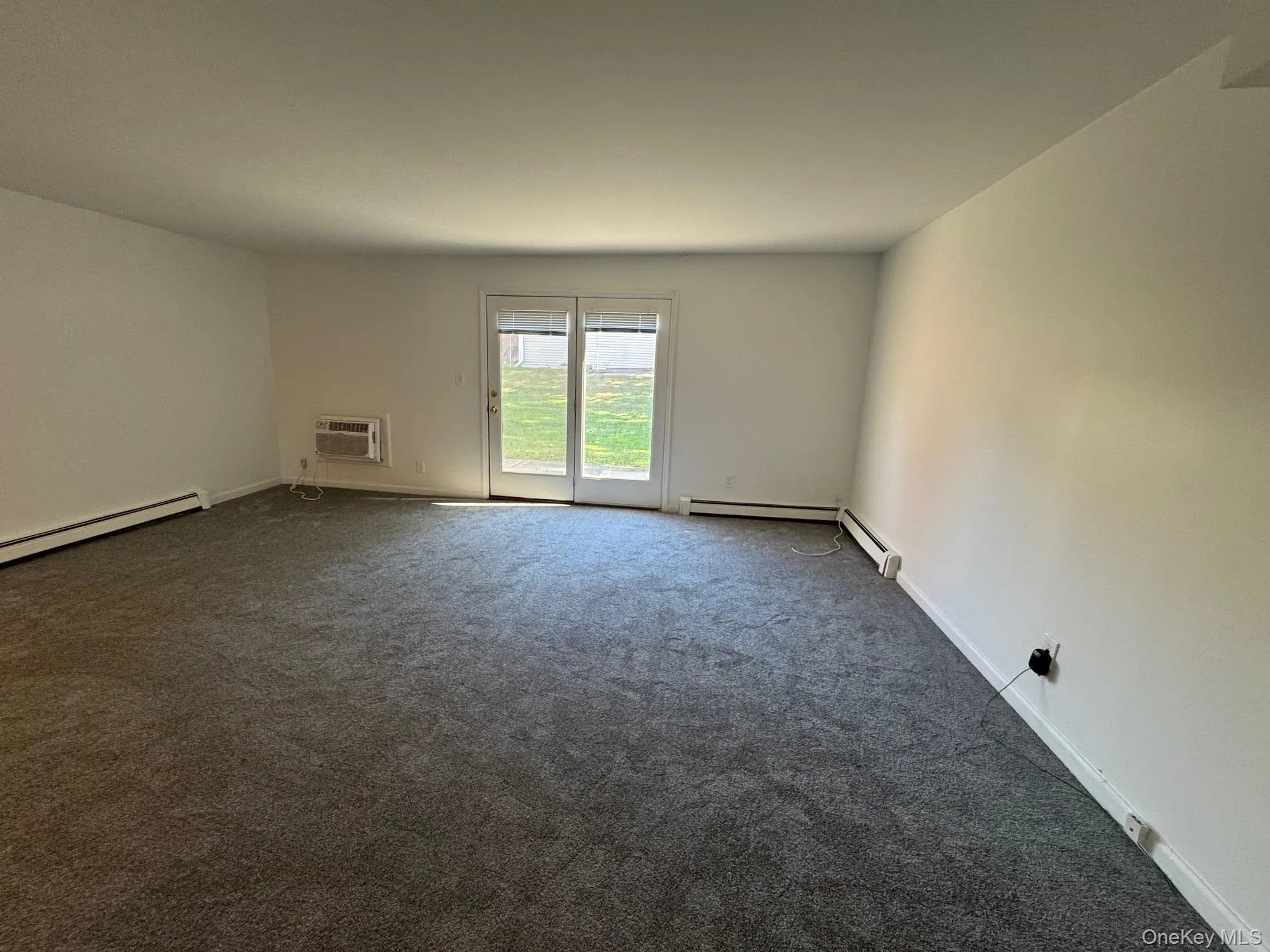 Carpeted spare room with baseboards and a wall mounted air conditioner Carpeted spare room with baseboards and a wall mounted air conditioner