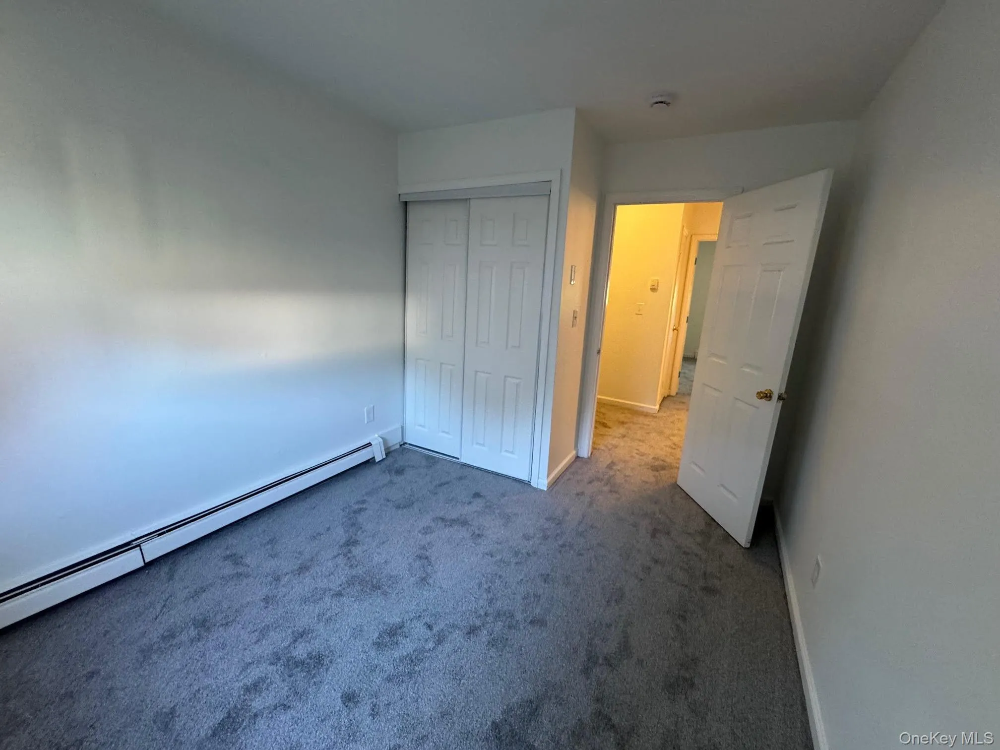 Unfurnished bedroom with carpet floors, a baseboard heating unit, and a closet Unfurnished bedroom with carpet floors, a baseboard heating unit, and a closet