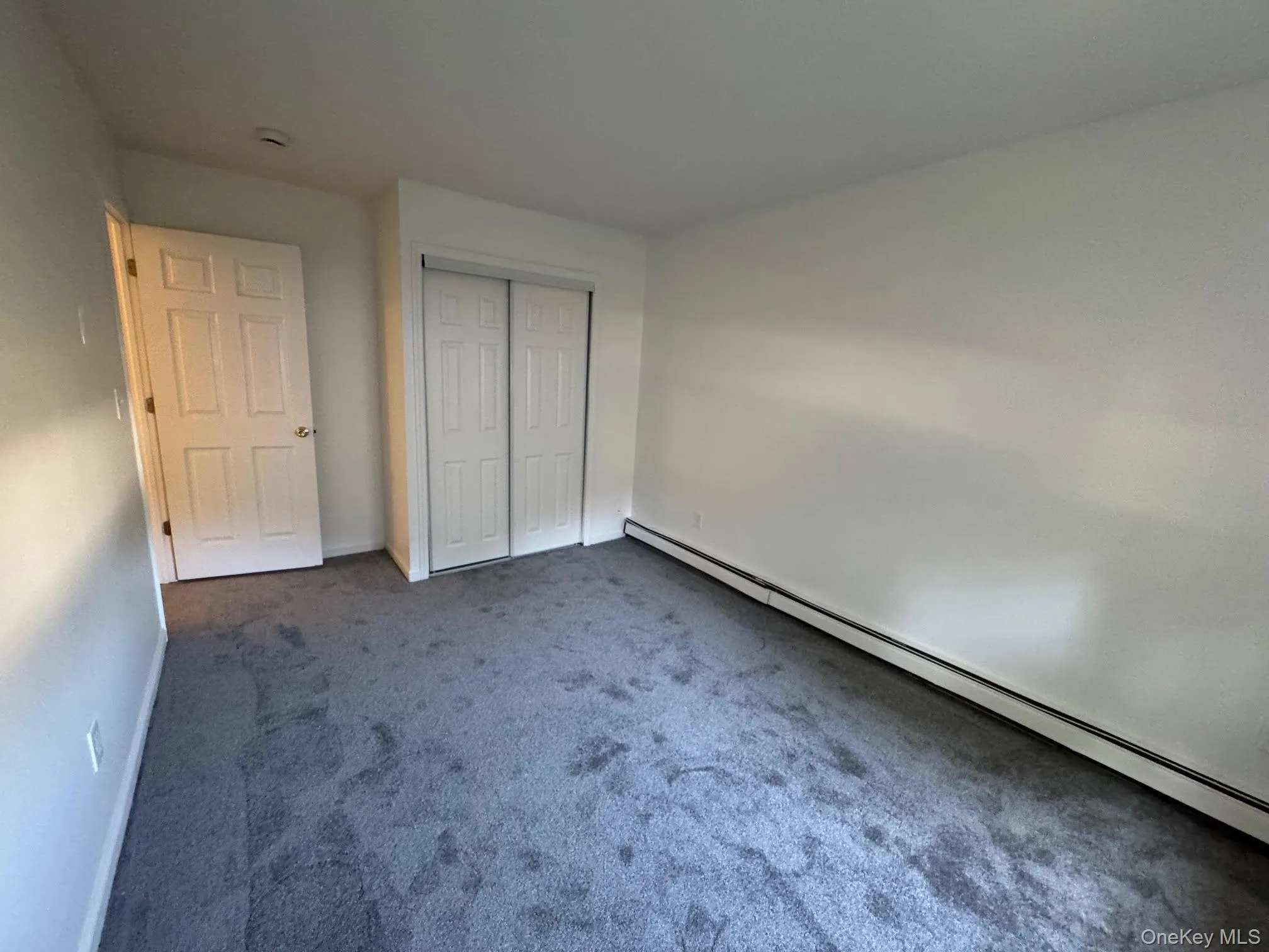 Unfurnished bedroom featuring a baseboard radiator, carpet, and a closet Unfurnished bedroom featuring a baseboard radiator, carpet, and a closet