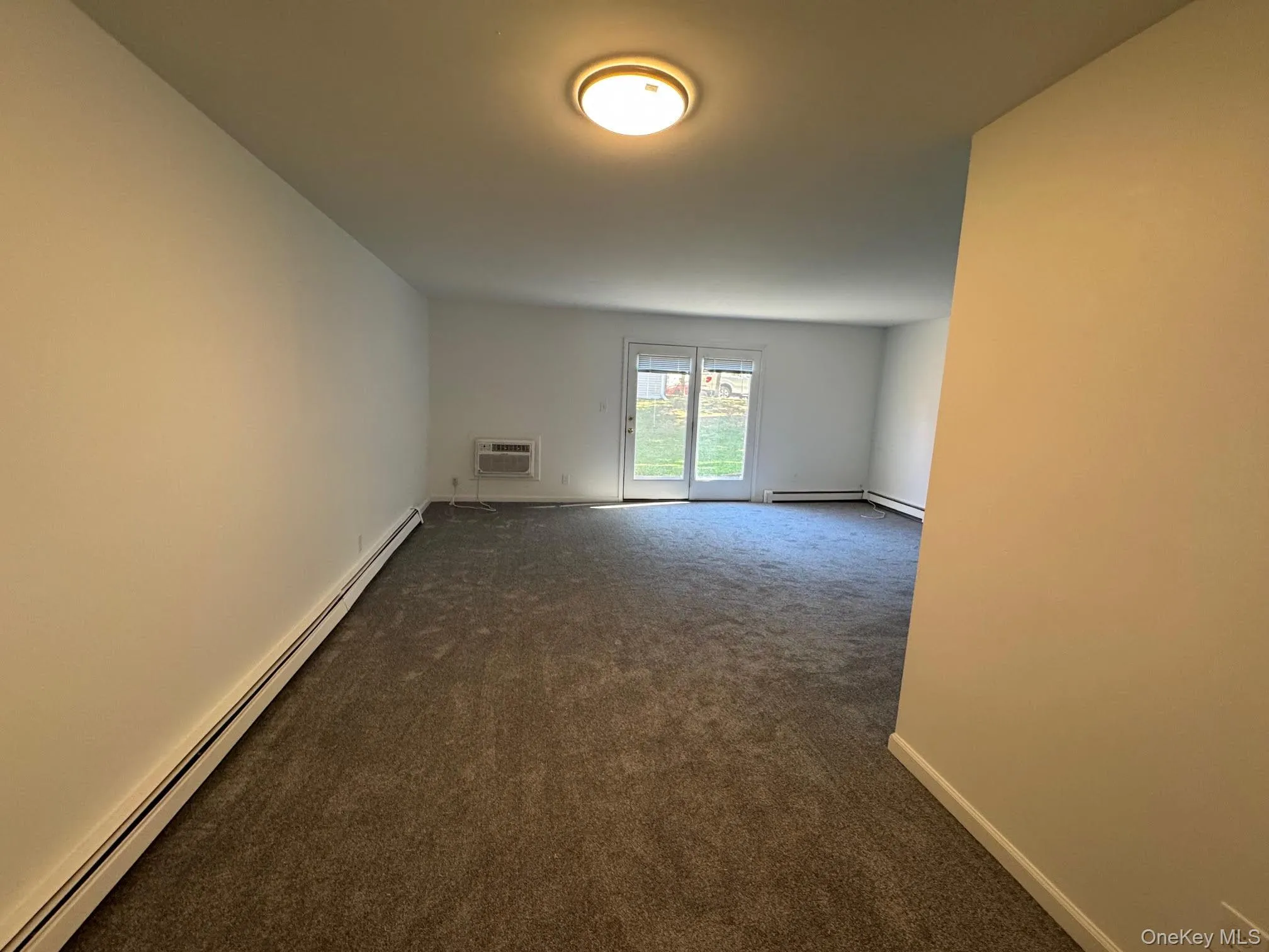 Unfurnished room with a baseboard heating unit, dark carpet, and a wall mounted air conditioner Unfurnished room with a baseboard heating unit, dark carpet, and a wall mounted air conditioner