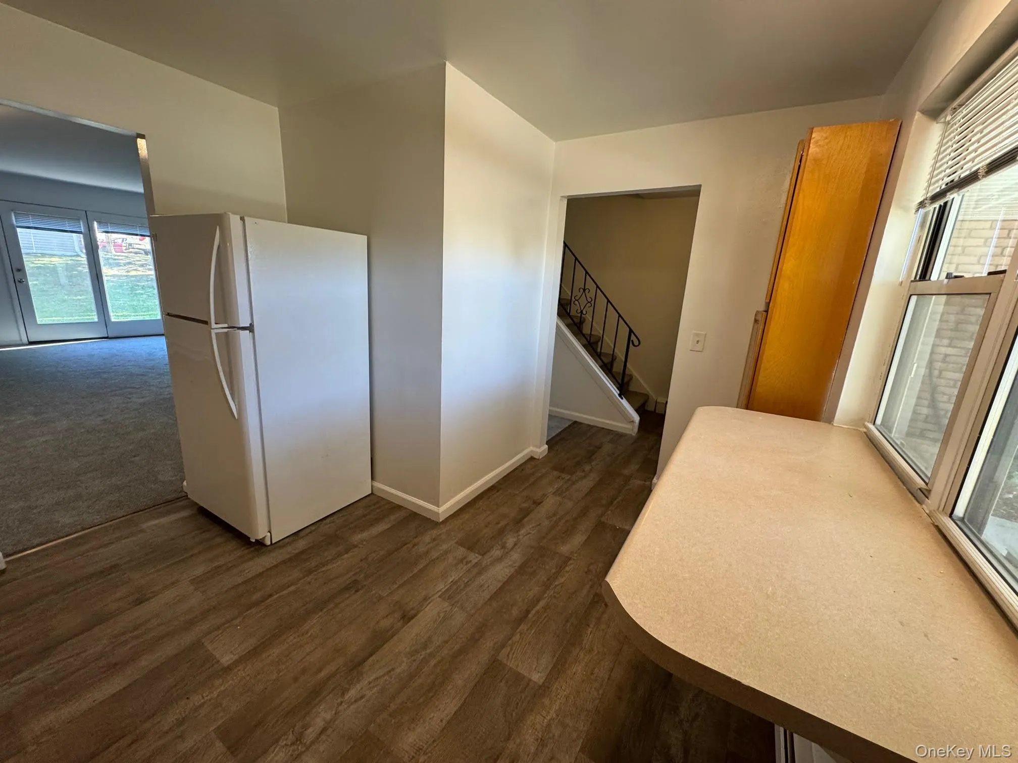 Kitchen featuring healthy amount of natural light, freestanding refrigerator, dark wood-style flooring, and light countertops Kitchen featuring healthy amount of natural light, freestanding refrigerator, dark wood-style flooring, and light countertops