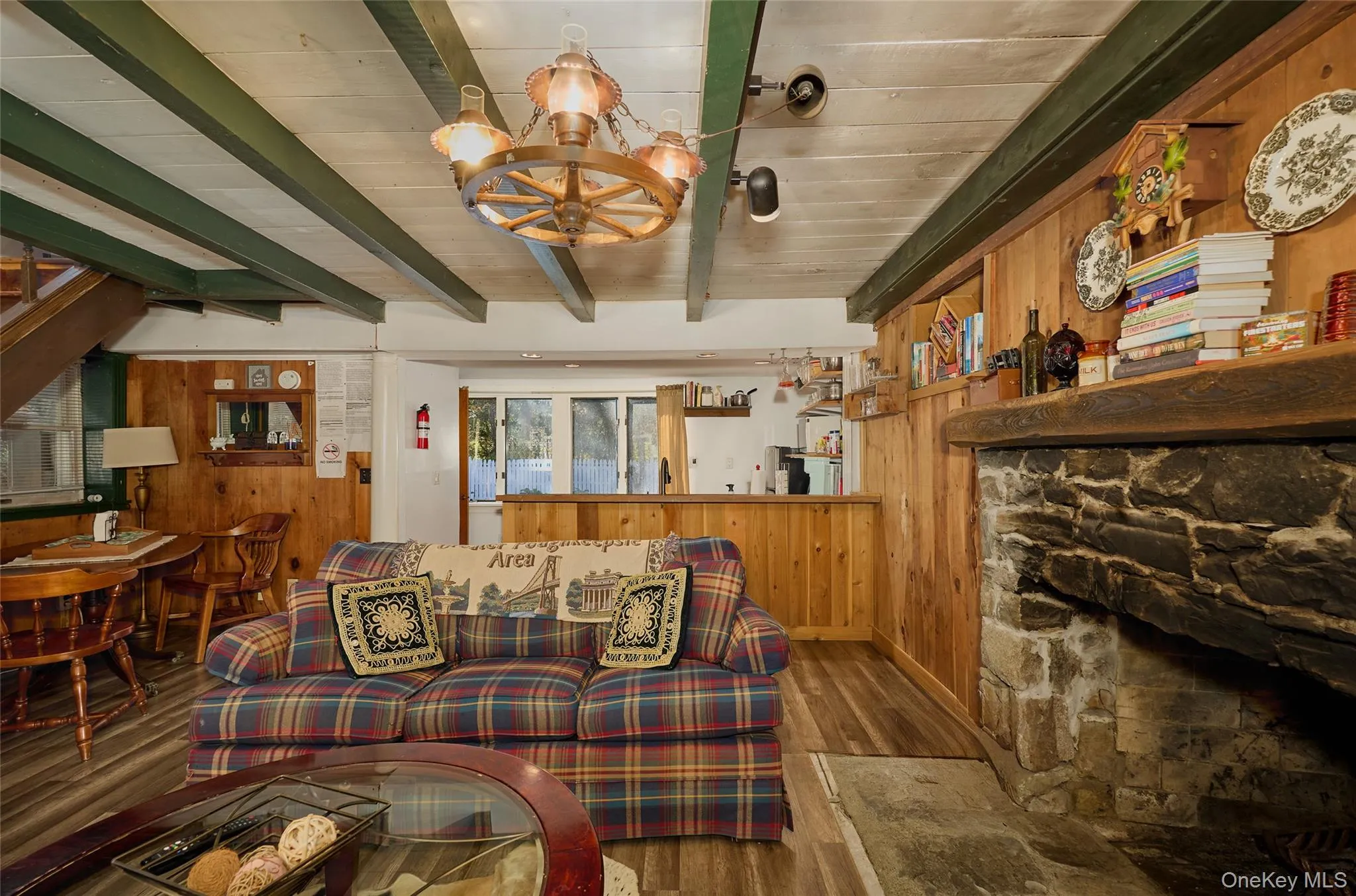 Cottage Living area featuring wood walls, a chandelier, beamed ceiling, wood finished floors, and a stone fireplace Cottage Living area featuring wood walls, a chandelier, beamed ceiling, wood finished floors, and a stone fireplace