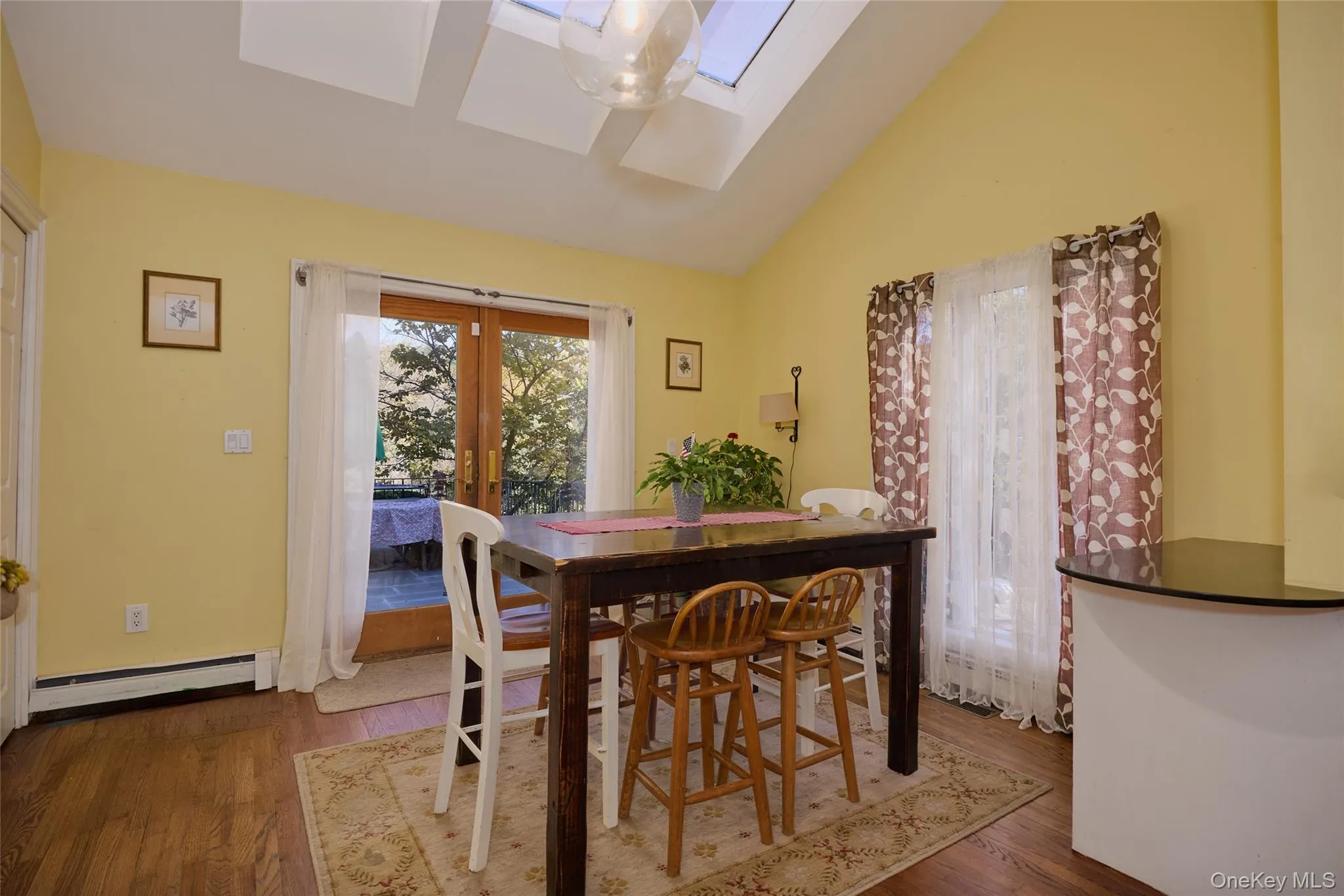 Dining space featuring french doors, vaulted ceiling, wood finished floors, a skylight, and a baseboard radiator Dining space featuring french doors, vaulted ceiling, wood finished floors, a skylight, and a baseboard radiator