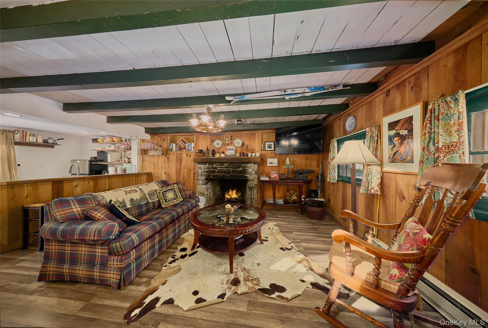 Cottage Living room with wood walls, baseboard heating, a fireplace, beamed ceiling, and wood finished floors Cottage Living room with wood walls, baseboard heating, a fireplace, beamed ceiling, and wood finished floors