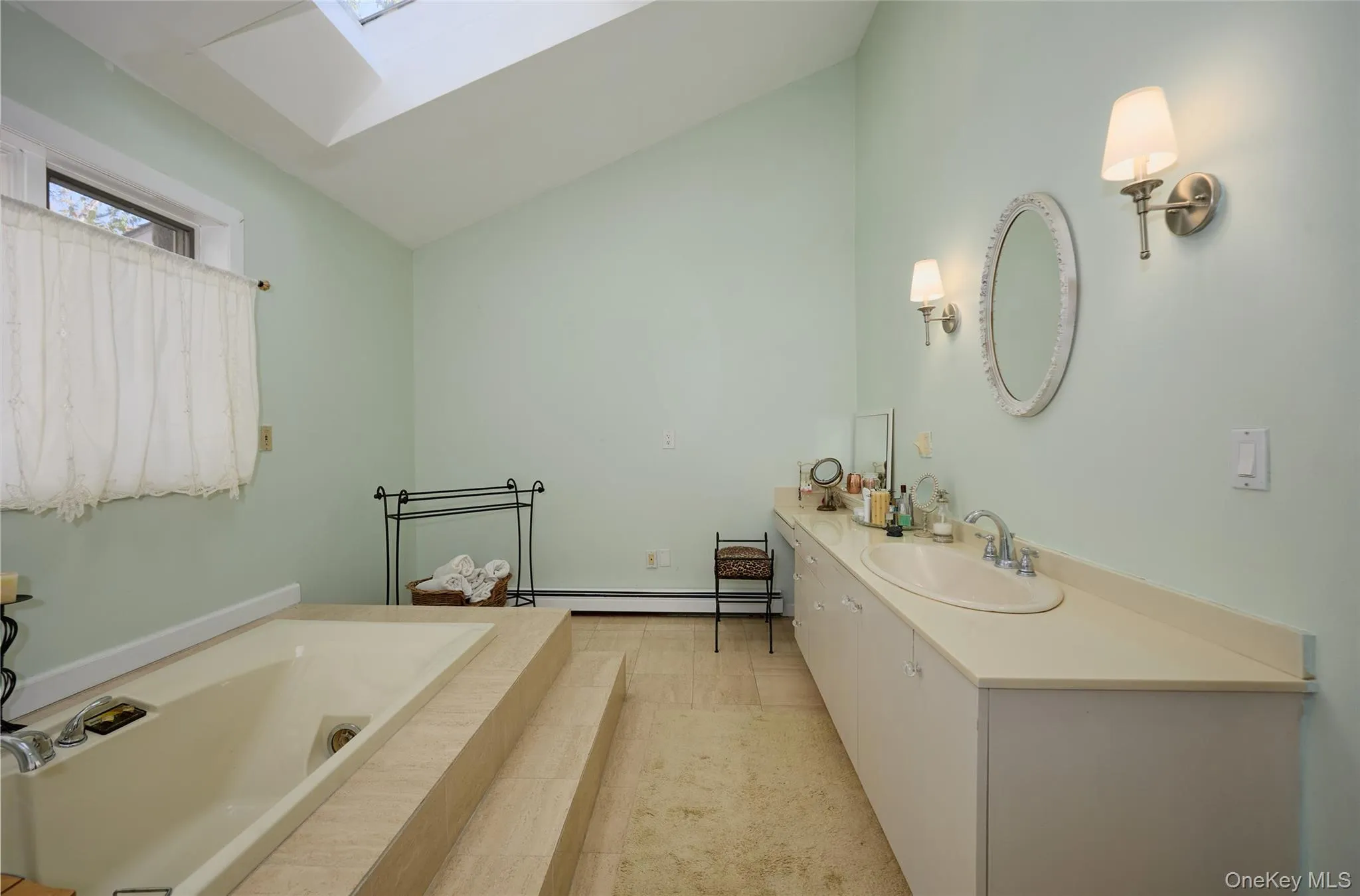Full bath featuring a skylight, a tub with jets, vanity, lofted ceiling, and baseboard heating Full bath featuring a skylight, a tub with jets, vanity, lofted ceiling, and baseboard heating