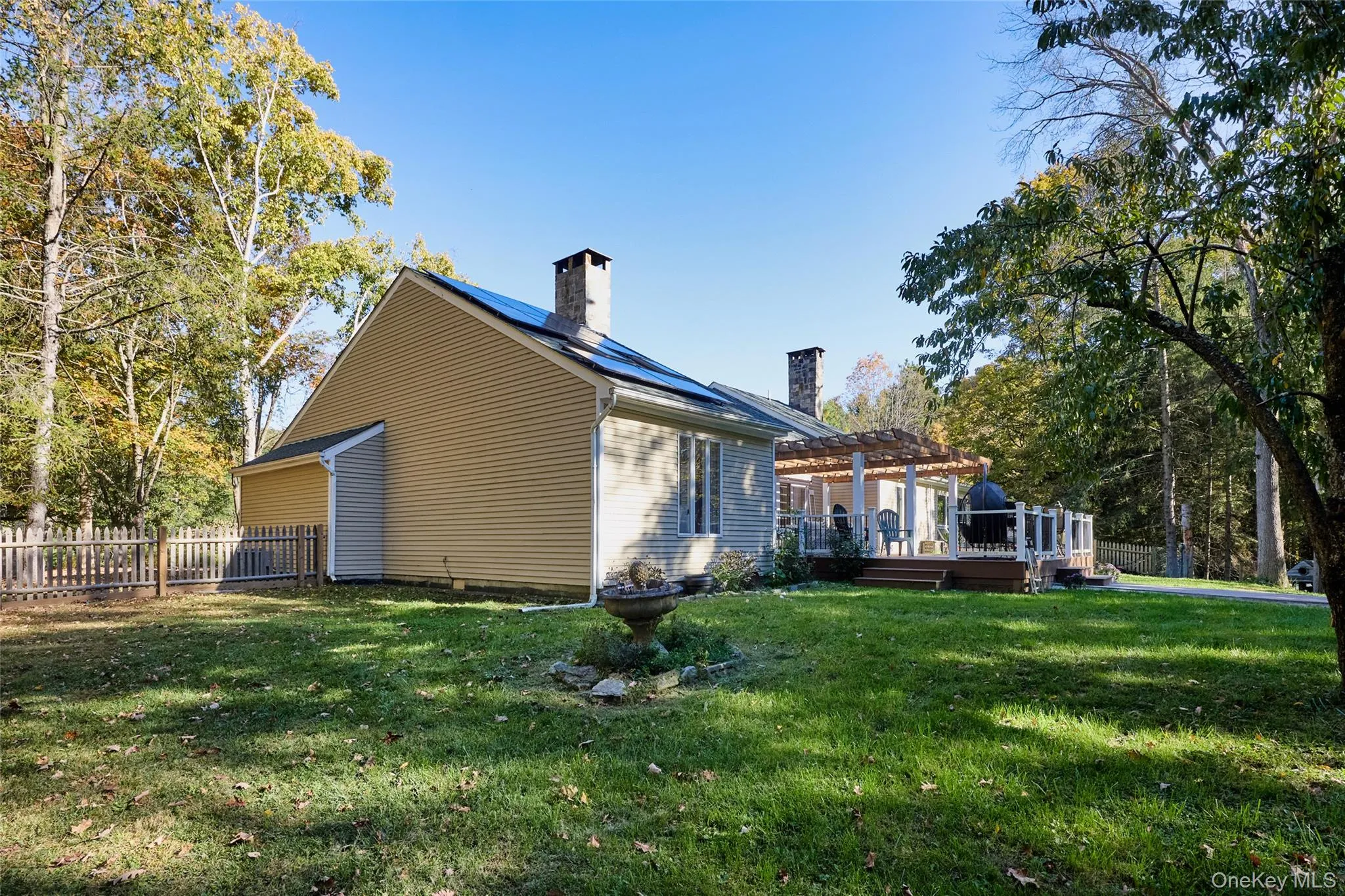 View of home's exterior with a deck, a lawn, a pergola, and a chimney View of home's exterior with a deck, a lawn, a pergola, and a chimney