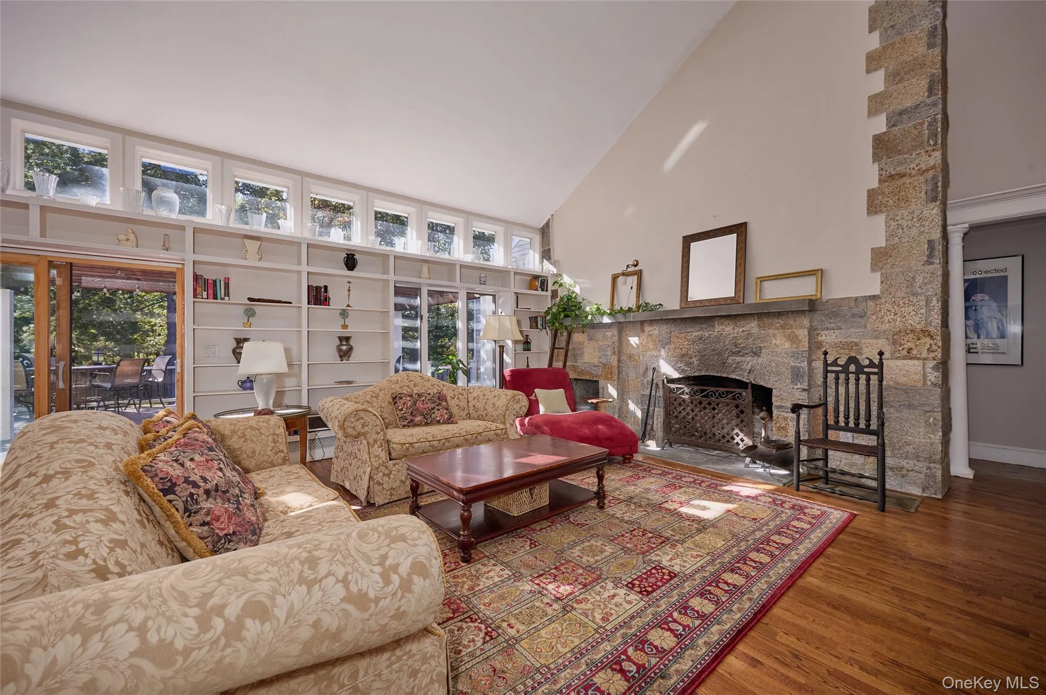 Living room featuring high vaulted ceiling, a stone fireplace, and wood finished floors Living room featuring high vaulted ceiling, a stone fireplace, and wood finished floors