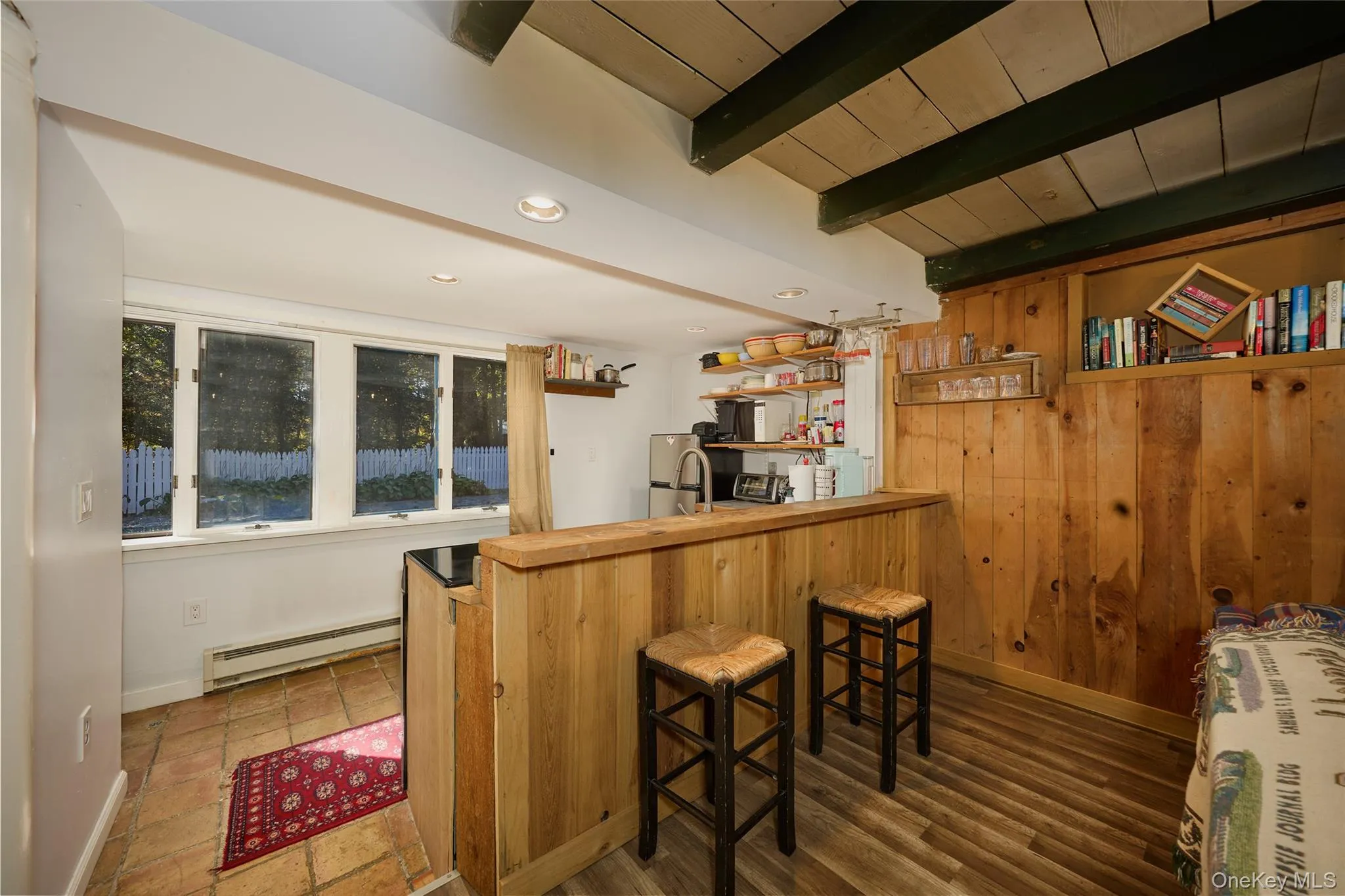 Cottage Kitchen with a breakfast bar, beamed ceiling, wood walls, a baseboard radiator, and open shelves Cottage Kitchen with a breakfast bar, beamed ceiling, wood walls, a baseboard radiator, and open shelves