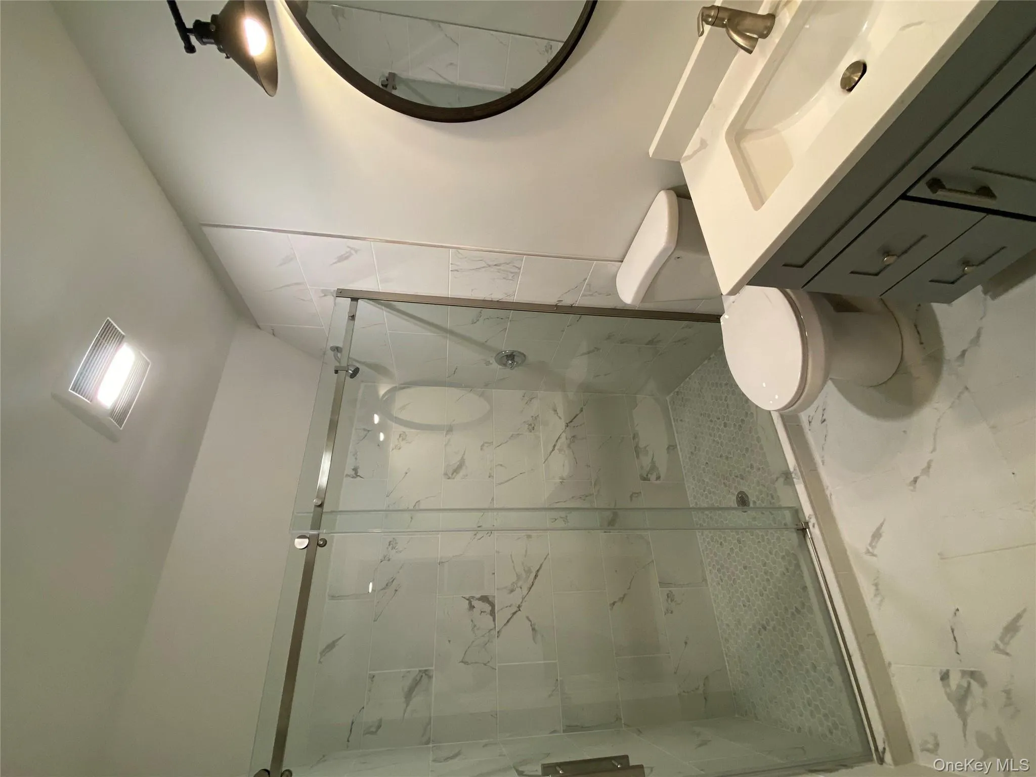 Primary full bath featuring a marble finish shower, light marble finish floors, vanity, and vaulted ceiling Primary full bath featuring a marble finish shower, light marble finish floors, vanity, and vaulted ceiling