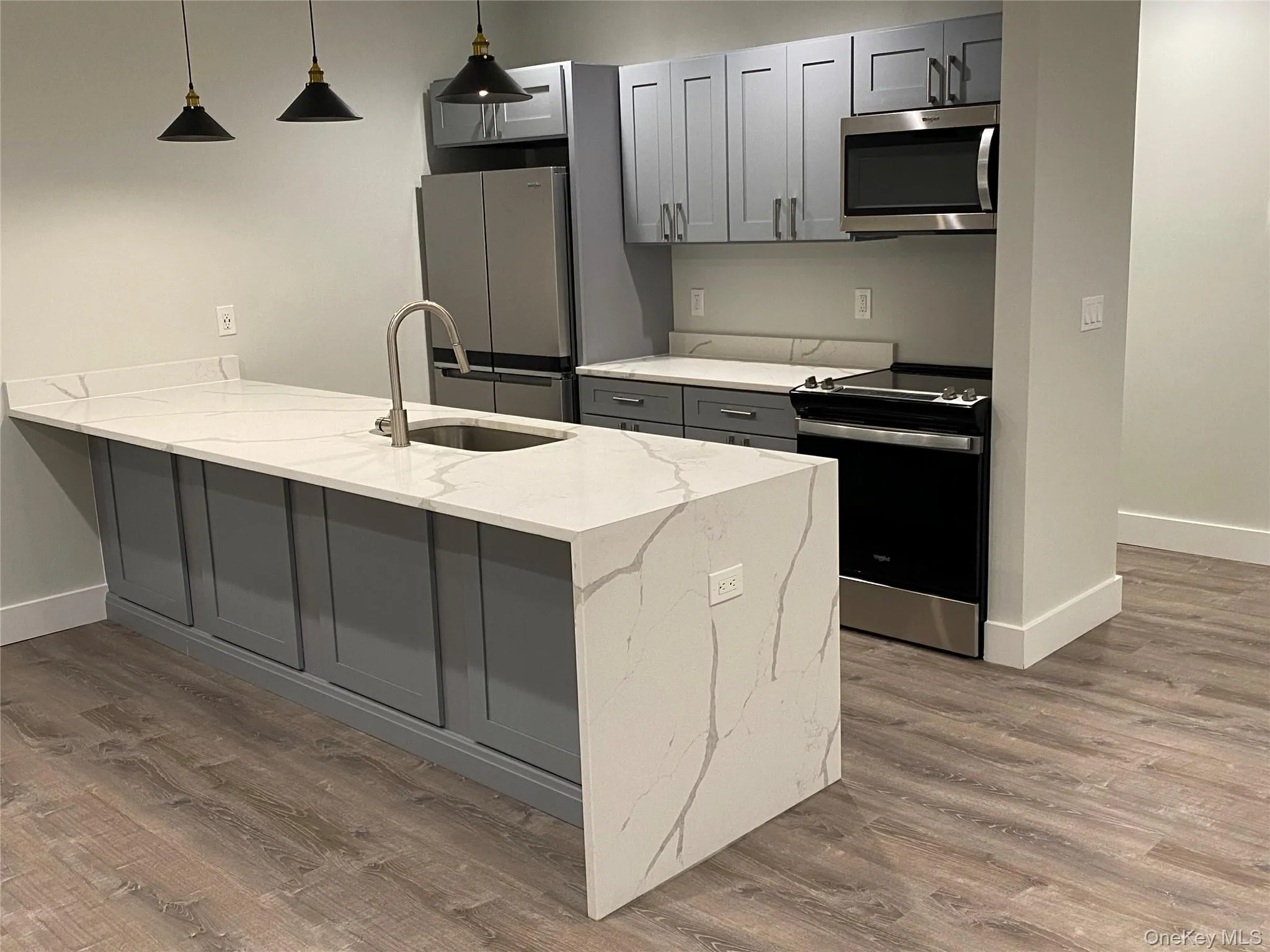 Kitchen featuring gray cabinets, stainless steel appliances, light stone counters, a peninsula, and hanging light fixtures Kitchen featuring gray cabinets, stainless steel appliances, light stone counters, a peninsula, and hanging light fixtures