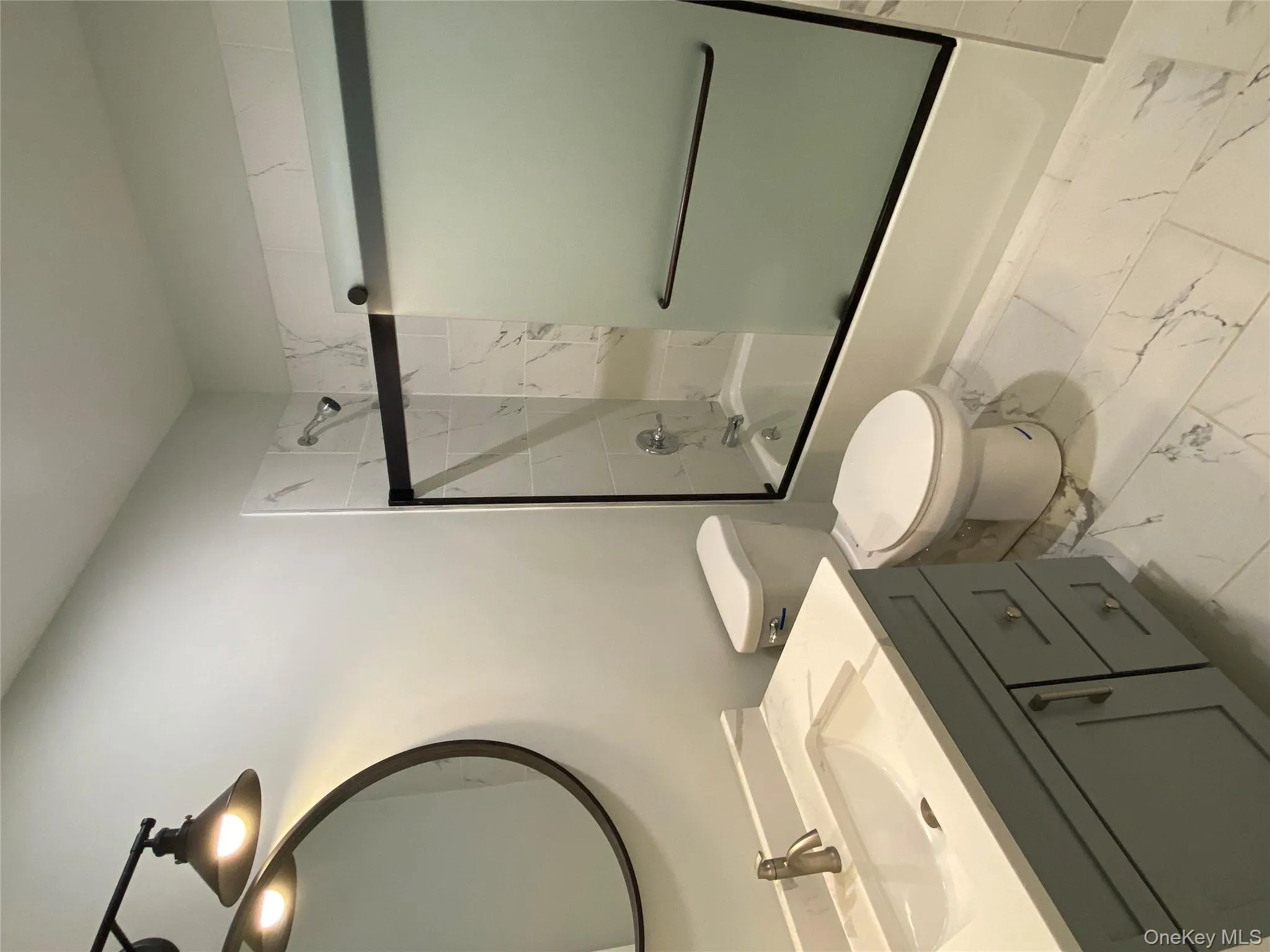 Hall full bathroom featuring shower / bath combination with glass door, vanity, and light marble finish floors Hall full bathroom featuring shower / bath combination with glass door, vanity, and light marble finish floors