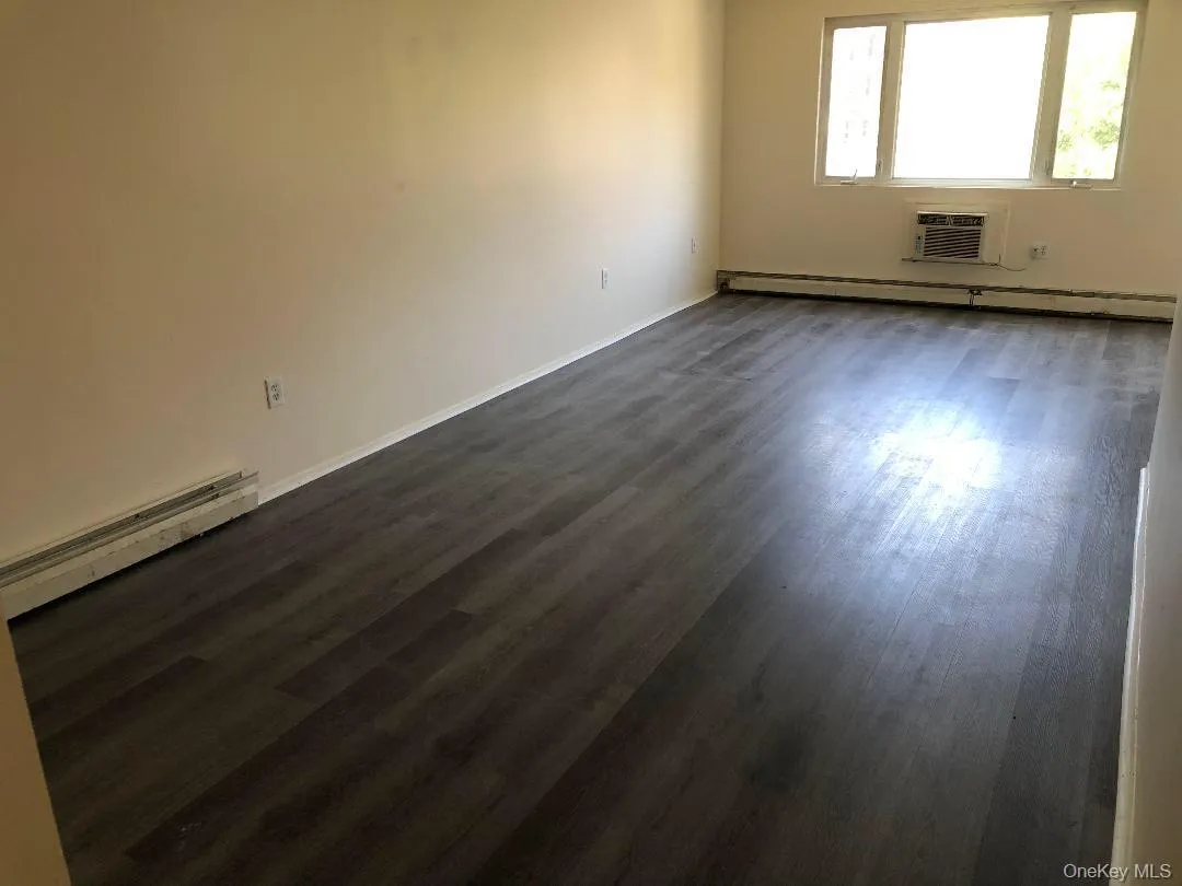 Empty room with a baseboard radiator, dark wood finished floors, and a wall mounted AC Empty room with a baseboard radiator, dark wood finished floors, and a wall mounted AC