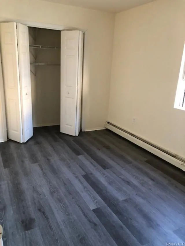 Unfurnished bedroom featuring a baseboard radiator, dark wood-style floors, and a closet Unfurnished bedroom featuring a baseboard radiator, dark wood-style floors, and a closet