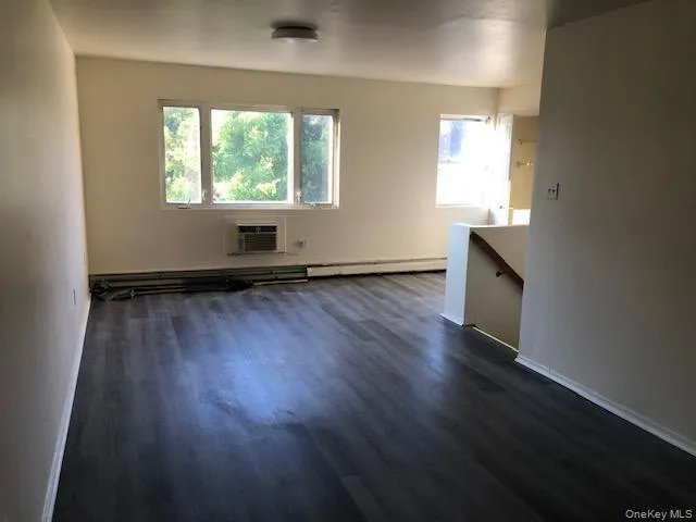 Unfurnished living room featuring dark wood-type flooring, baseboard heating, and a wall unit AC Unfurnished living room featuring dark wood-type flooring, baseboard heating, and a wall unit AC