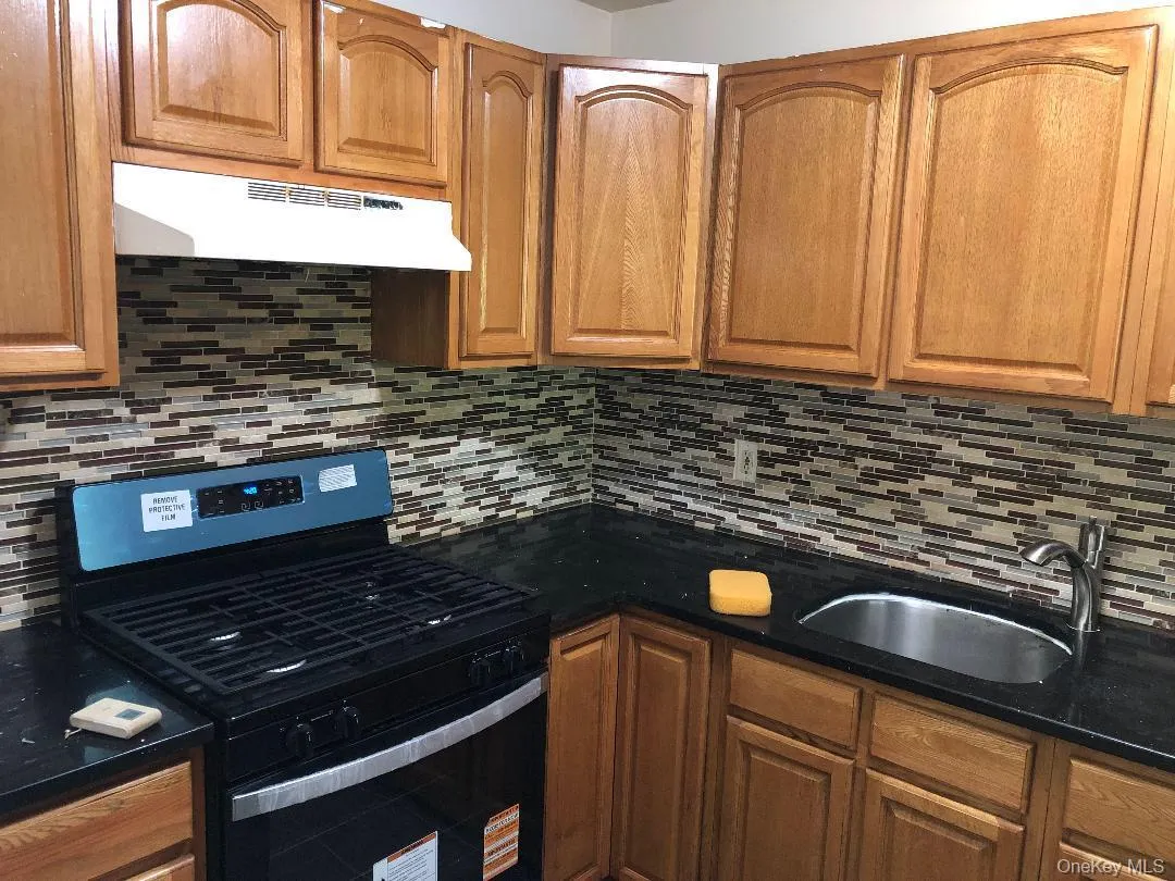 Kitchen with gas range, brown cabinets, dark stone counters, and under cabinet range hood Kitchen with gas range, brown cabinets, dark stone counters, and under cabinet range hood