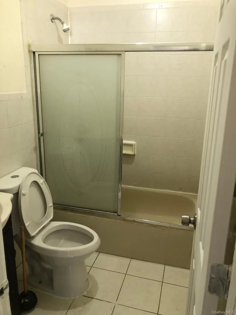 Full bath featuring light tile patterned flooring, bath / shower combo with glass door, tile walls, and vanity Full bath featuring light tile patterned flooring, bath / shower combo with glass door, tile walls, and vanity