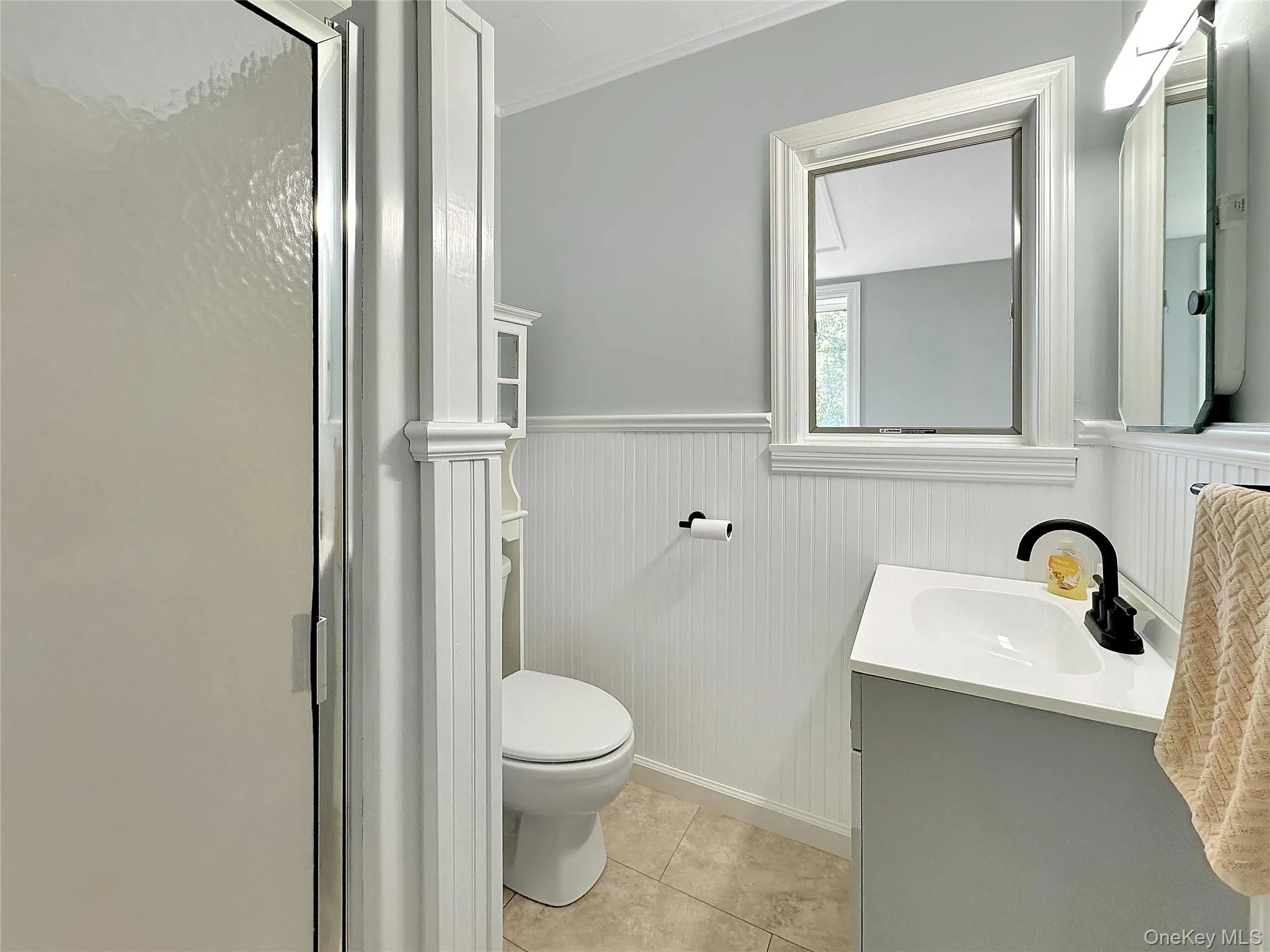 Bathroom featuring wainscoting, vanity, a shower stall, light tile patterned floors, and crown molding Bathroom featuring wainscoting, vanity, a shower stall, light tile patterned floors, and crown molding