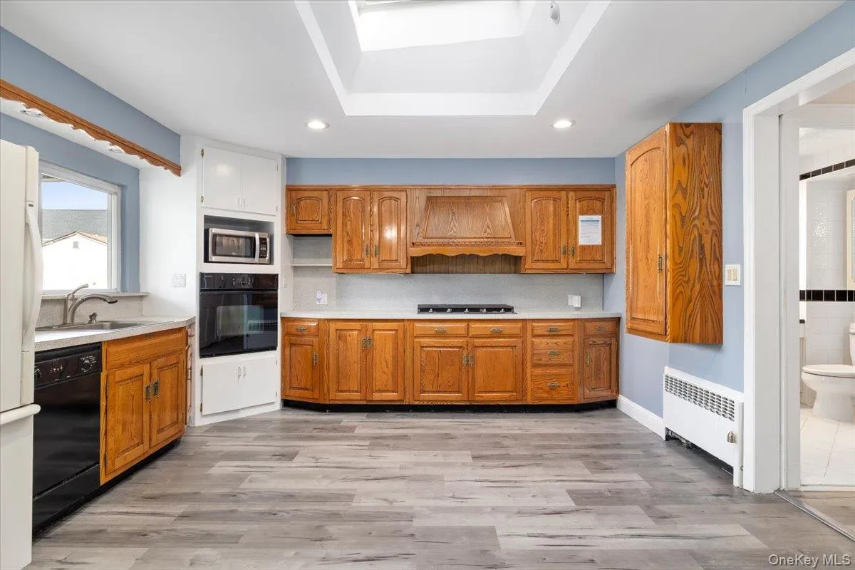 Kitchen with light countertops, black appliances, radiator, light wood finished floors, and a raised ceiling Kitchen with light countertops, black appliances, radiator, light wood finished floors, and a raised ceiling