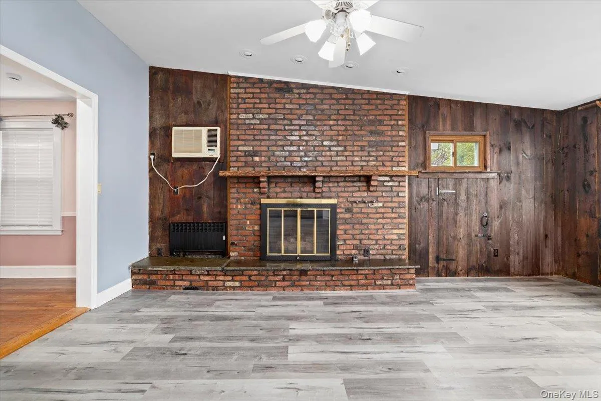 Unfurnished living room with wood walls, a fireplace, wood finished floors, a ceiling fan, and vaulted ceiling Unfurnished living room with wood walls, a fireplace, wood finished floors, a ceiling fan, and vaulted ceiling