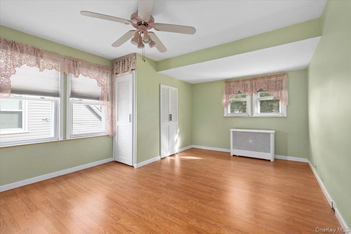 Empty room with radiator heating unit, light wood-style flooring, and a ceiling fan Empty room with radiator heating unit, light wood-style flooring, and a ceiling fan