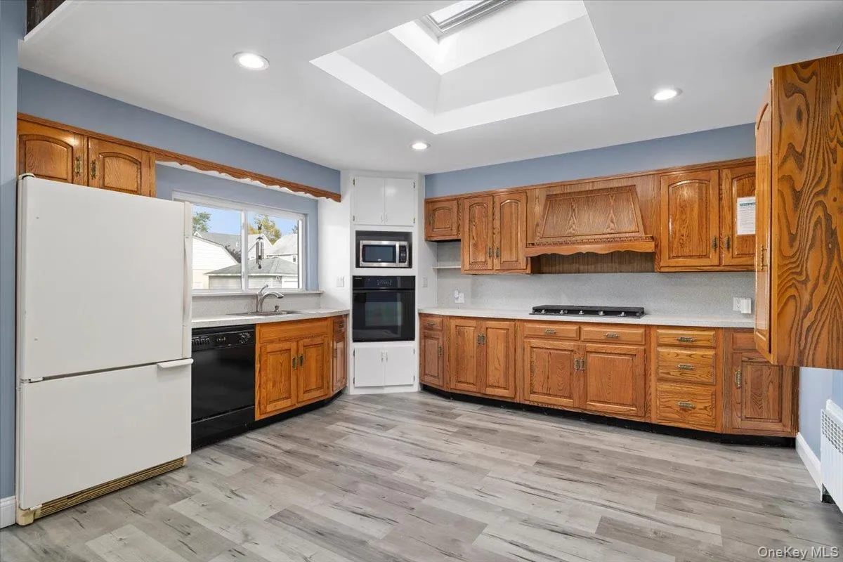Kitchen featuring black appliances, light countertops, a skylight, light wood-type flooring, and brown cabinets Kitchen featuring black appliances, light countertops, a skylight, light wood-type flooring, and brown cabinets