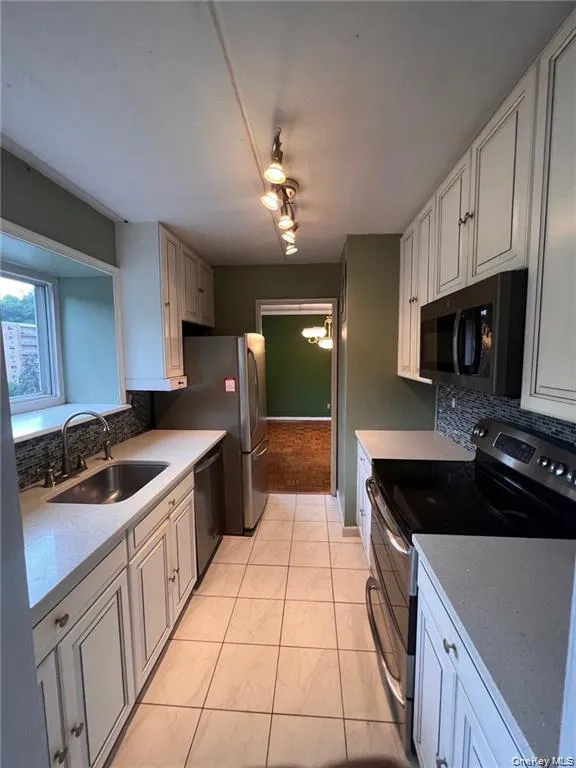 Kitchen with tasteful backsplash, stainless steel appliances, light stone countertops, light tile patterned flooring, and white cabinetry Kitchen with tasteful backsplash, stainless steel appliances, light stone countertops, light tile patterned flooring, and white cabinetry
