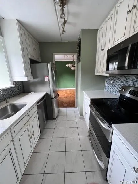 Kitchen with tasteful backsplash, stainless steel appliances, and white cabinetry Kitchen with tasteful backsplash, stainless steel appliances, and white cabinetry