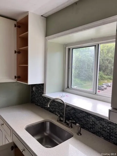 Kitchen with open shelves, decorative backsplash, white cabinetry, and light stone countertops Kitchen with open shelves, decorative backsplash, white cabinetry, and light stone countertops