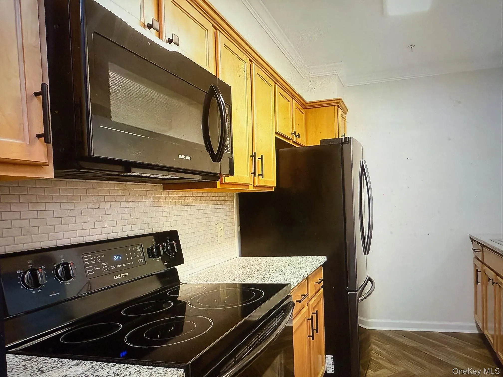 Kitchen with black appliances, backsplash, ornamental molding, light stone countertops, and brown cabinetry Kitchen with black appliances, backsplash, ornamental molding, light stone countertops, and brown cabinetry