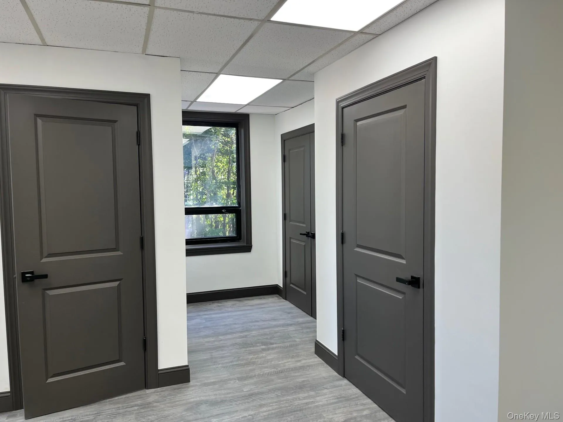 Corridor featuring a paneled ceiling and light wood-type flooring Corridor featuring a paneled ceiling and light wood-type flooring