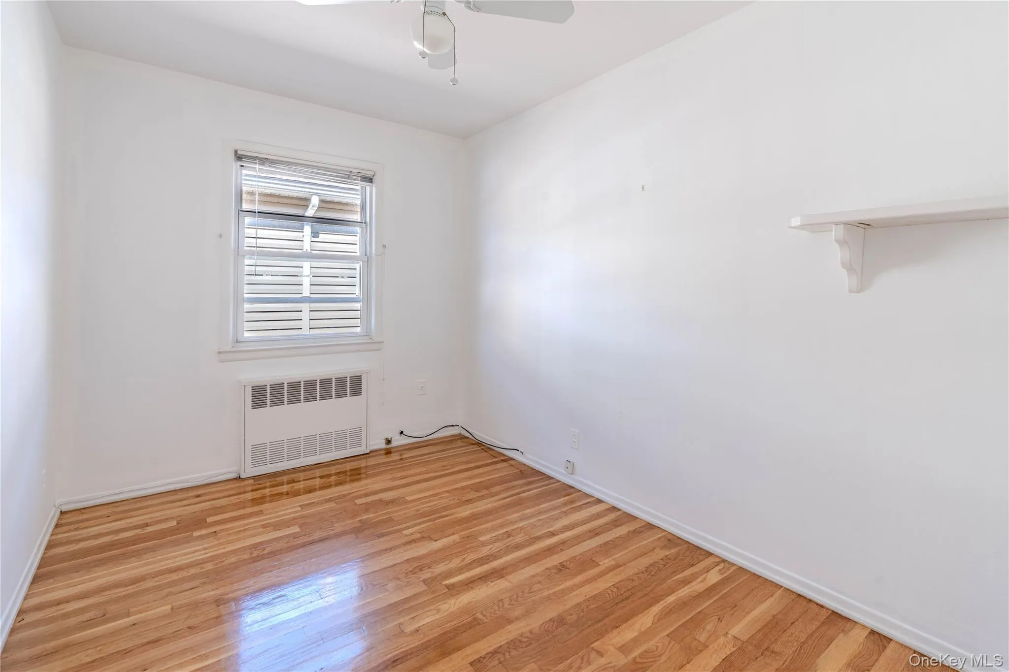 Empty room with radiator, light wood-style floors, and ceiling fan Empty room with radiator, light wood-style floors, and ceiling fan