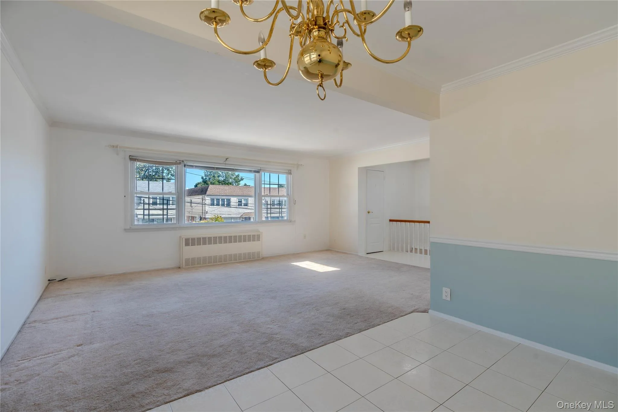 Empty room with light colored carpet, ornamental molding, light tile patterned floors, radiator heating unit, and a chandelier Empty room with light colored carpet, ornamental molding, light tile patterned floors, radiator heating unit, and a chandelier