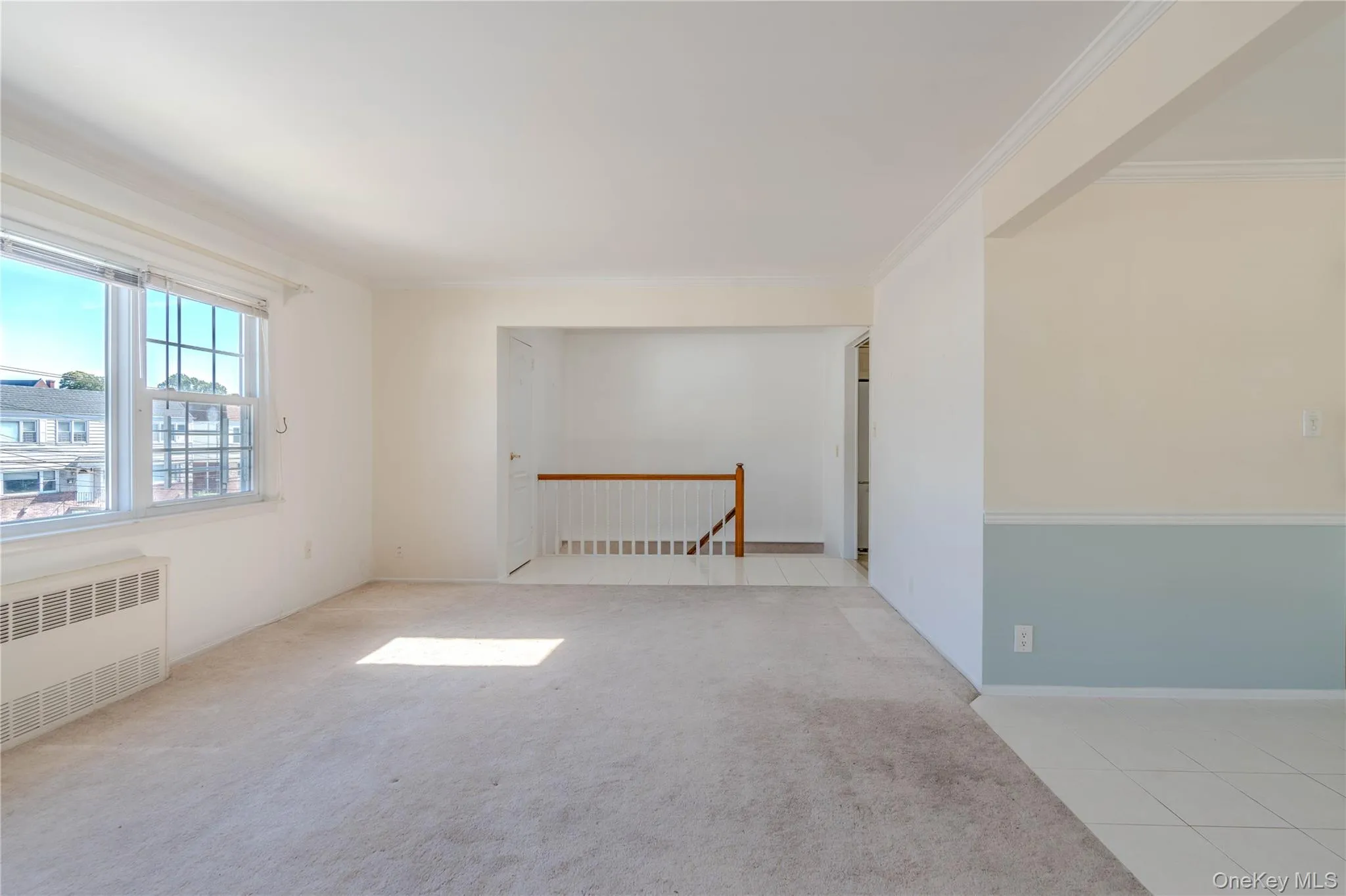 Empty room with light colored carpet, radiator, light tile patterned floors, and crown molding Empty room with light colored carpet, radiator, light tile patterned floors, and crown molding