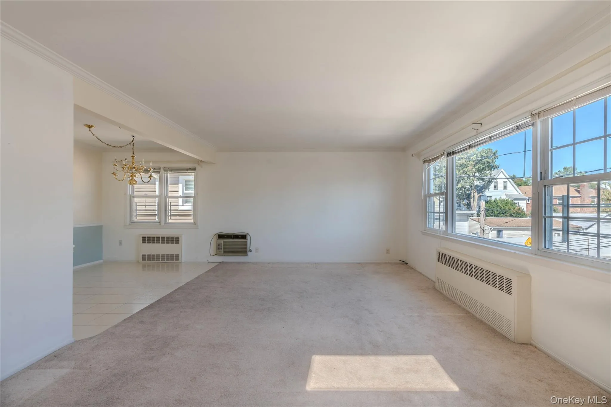 Spare room with light colored carpet, radiator, a chandelier, light tile patterned floors, and crown molding Spare room with light colored carpet, radiator, a chandelier, light tile patterned floors, and crown molding