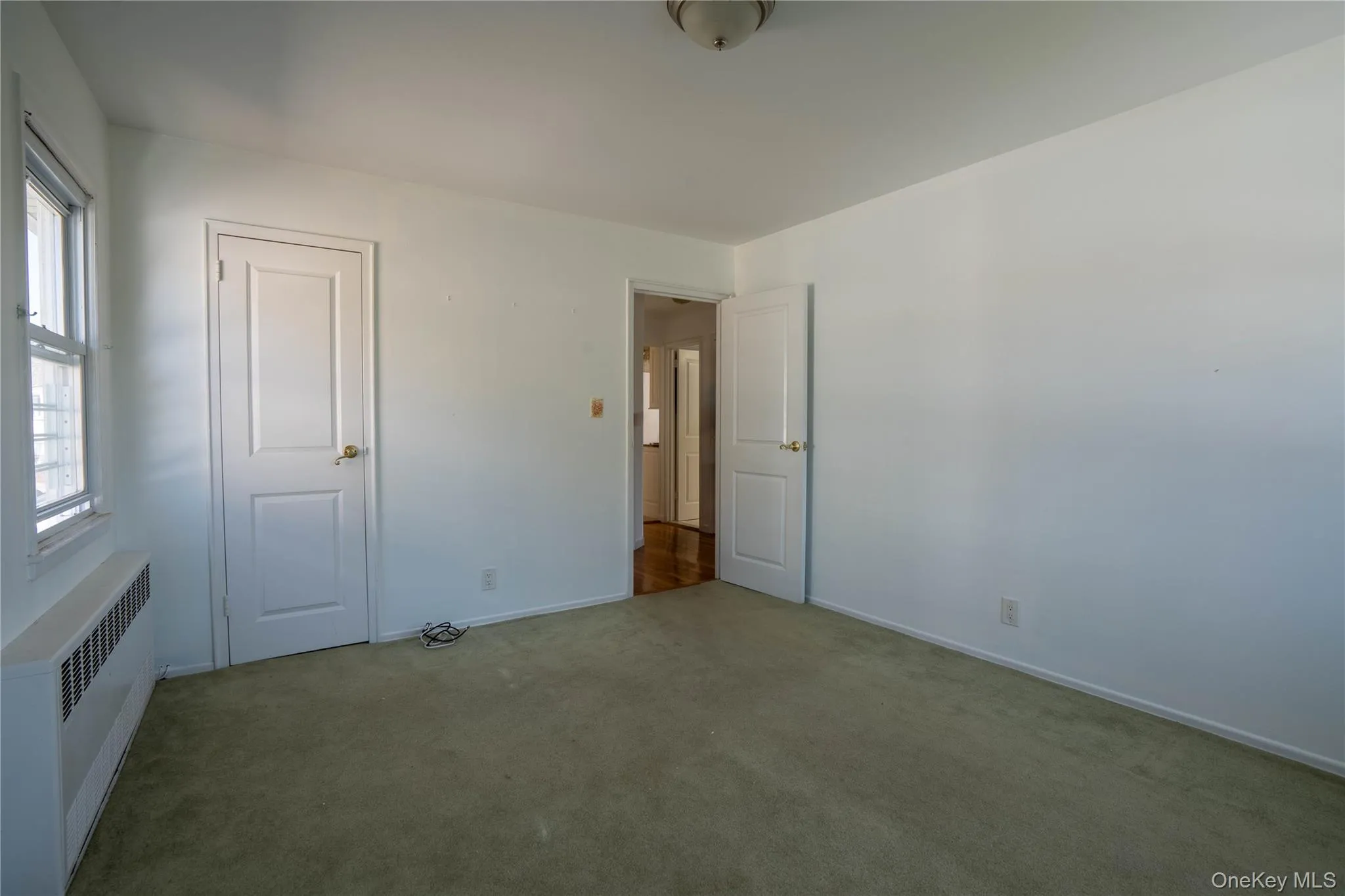 Unfurnished bedroom featuring radiator heating unit and carpet floors Unfurnished bedroom featuring radiator heating unit and carpet floors