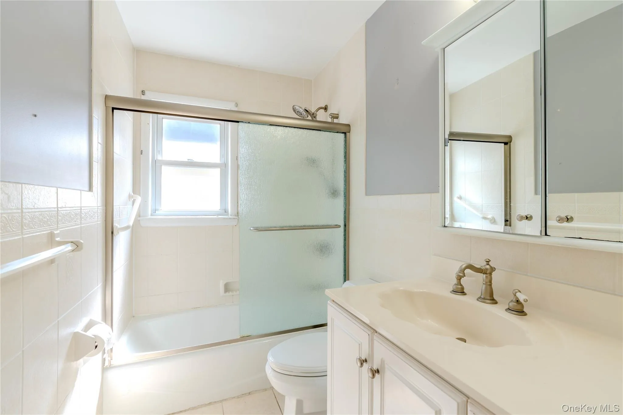 Full bathroom with tile walls, vanity, bath / shower combo with glass door, light tile patterned floors, and backsplash Full bathroom with tile walls, vanity, bath / shower combo with glass door, light tile patterned floors, and backsplash