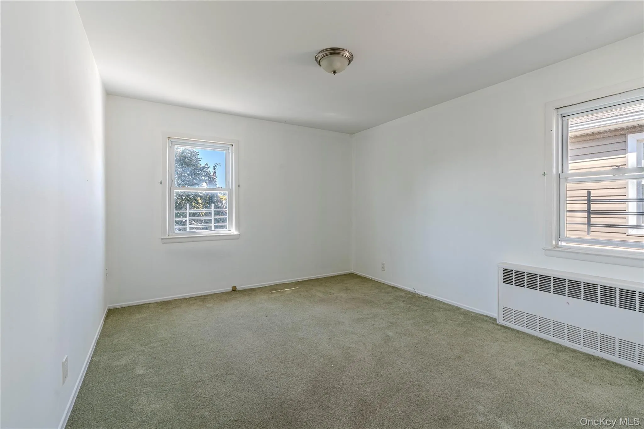 Carpeted spare room featuring radiator heating unit and baseboards Carpeted spare room featuring radiator heating unit and baseboards