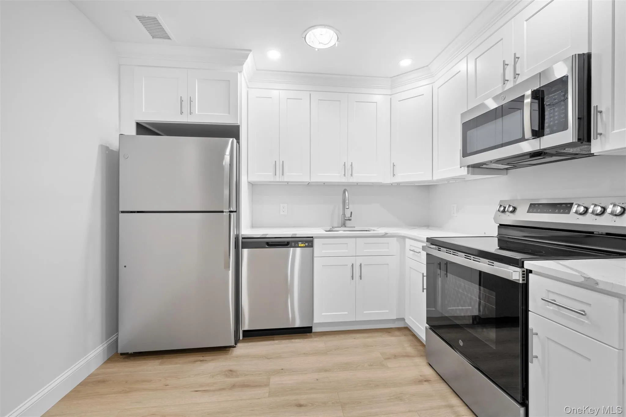 Kitchen featuring appliances with stainless steel finishes, light wood-type flooring, white cabinetry, light stone countertops, and recessed lighting Kitchen featuring appliances with stainless steel finishes, light wood-type flooring, white cabinetry, light stone countertops, and recessed lighting