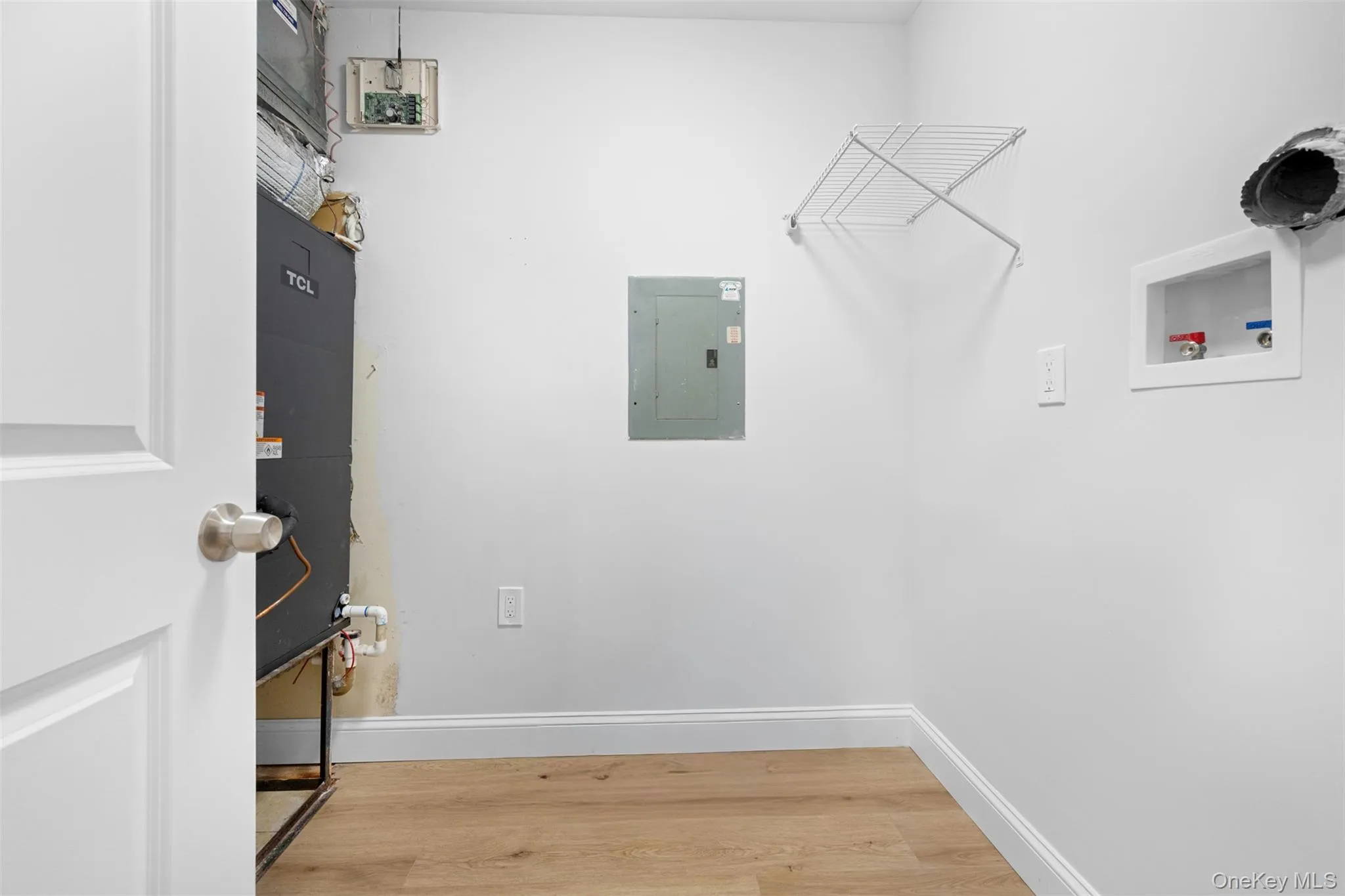 Washroom with light wood-style flooring, electric panel, heating unit, and hookup for a washing machine Washroom with light wood-style flooring, electric panel, heating unit, and hookup for a washing machine