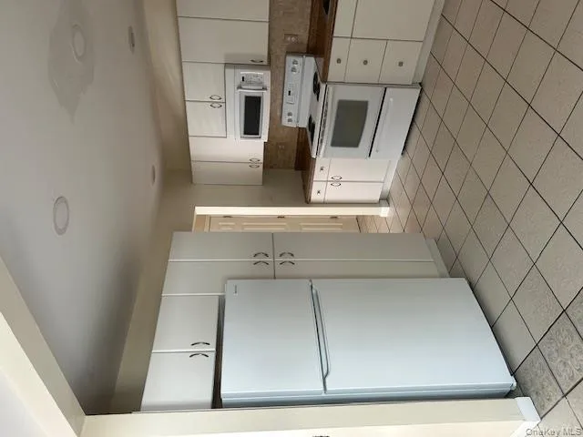 Kitchen with fridge, range, dark countertops, and white cabinetry Kitchen with fridge, range, dark countertops, and white cabinetry