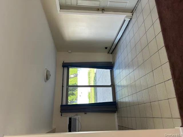 Unfurnished room with a baseboard heating unit, light tile patterned floors, and an AC wall unit Unfurnished room with a baseboard heating unit, light tile patterned floors, and an AC wall unit