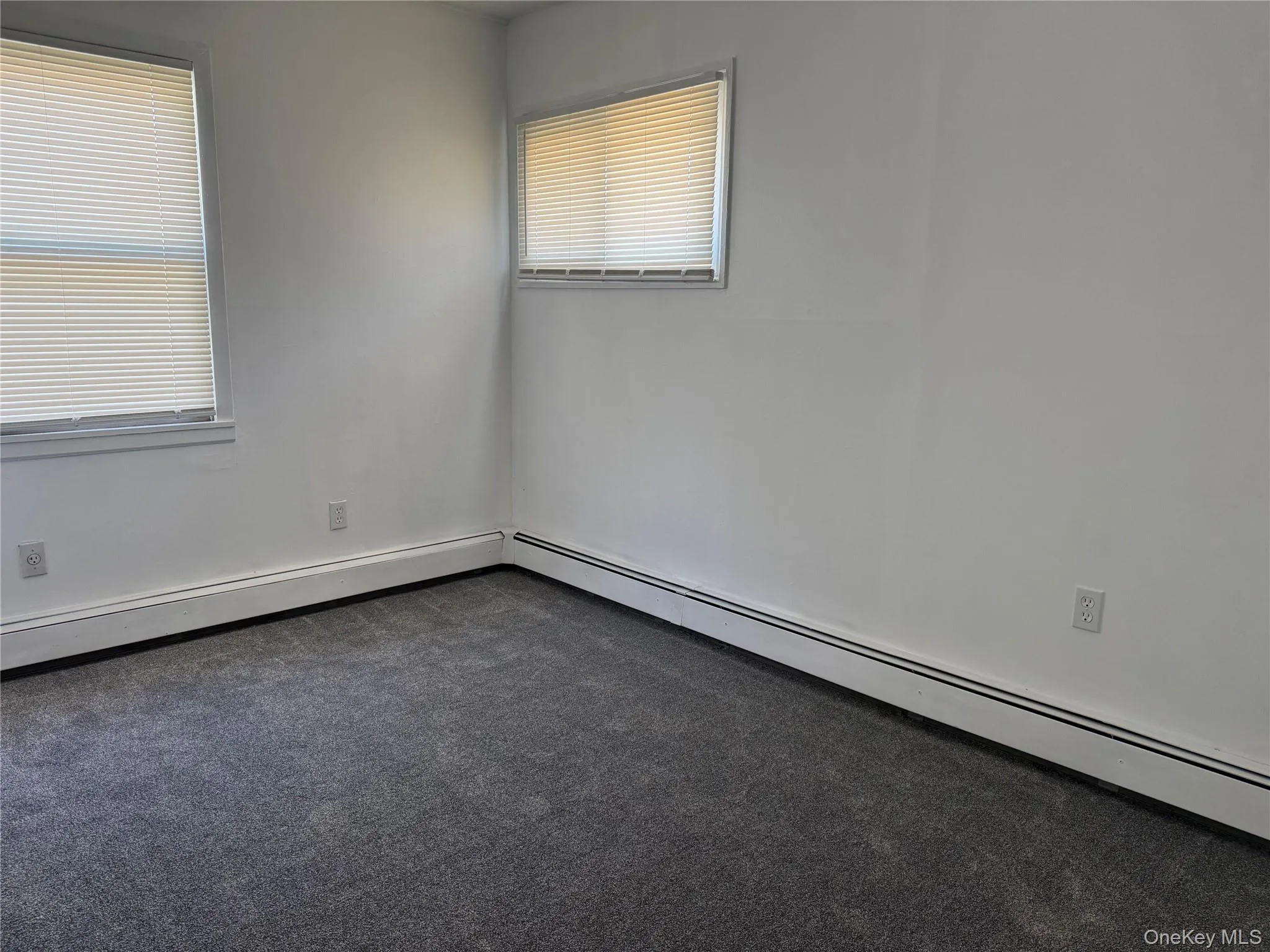 Spare room with baseboard heating and dark colored carpet Spare room with baseboard heating and dark colored carpet