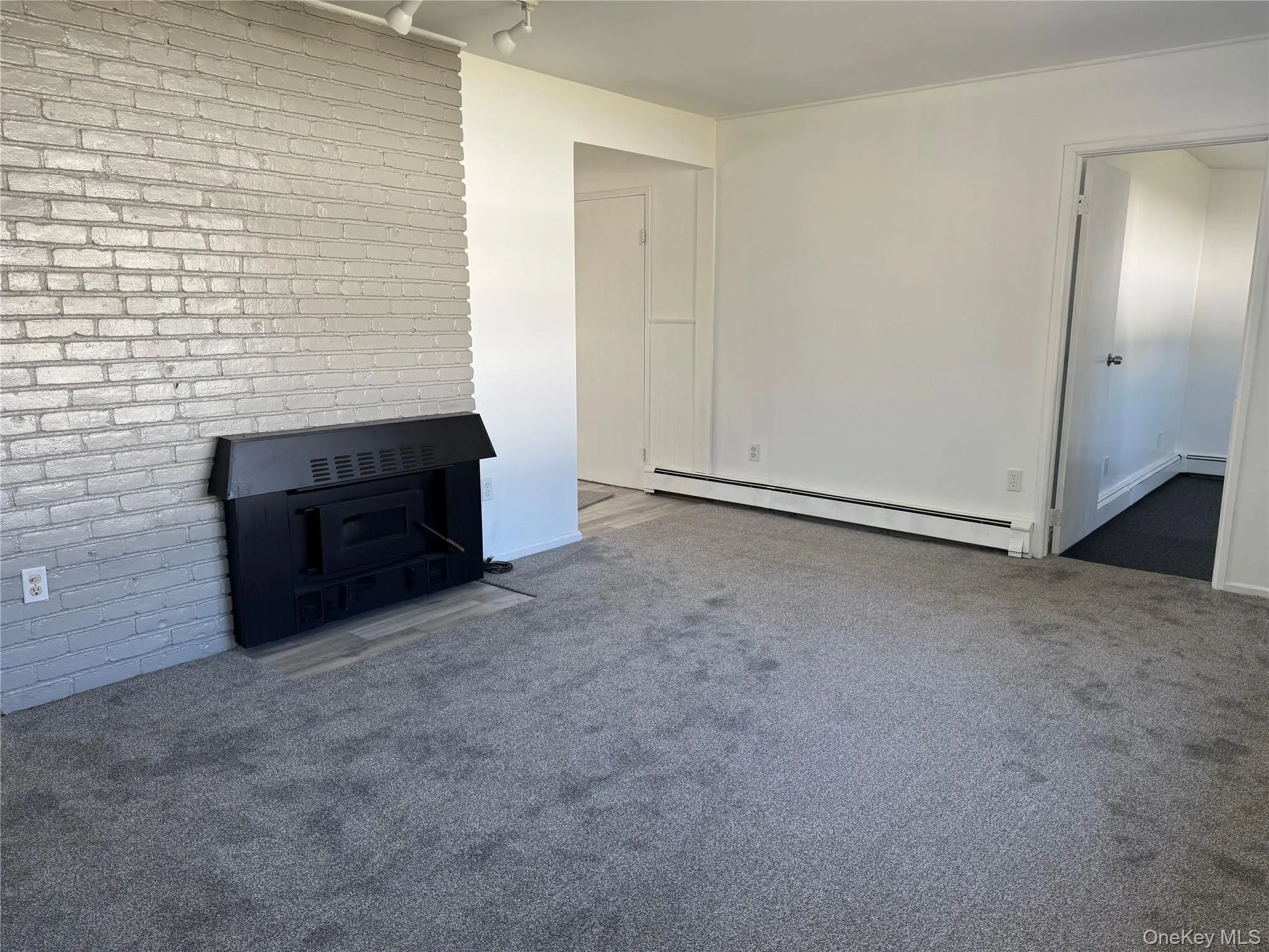 Unfurnished living room featuring a baseboard radiator, carpet flooring, brick wall, and a fireplace Unfurnished living room featuring a baseboard radiator, carpet flooring, brick wall, and a fireplace