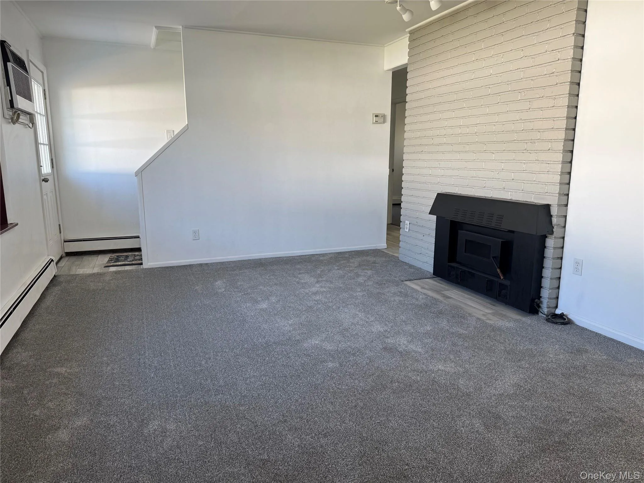 Unfurnished living room with a fireplace with flush hearth, carpet floors, and baseboard heating Unfurnished living room with a fireplace with flush hearth, carpet floors, and baseboard heating
