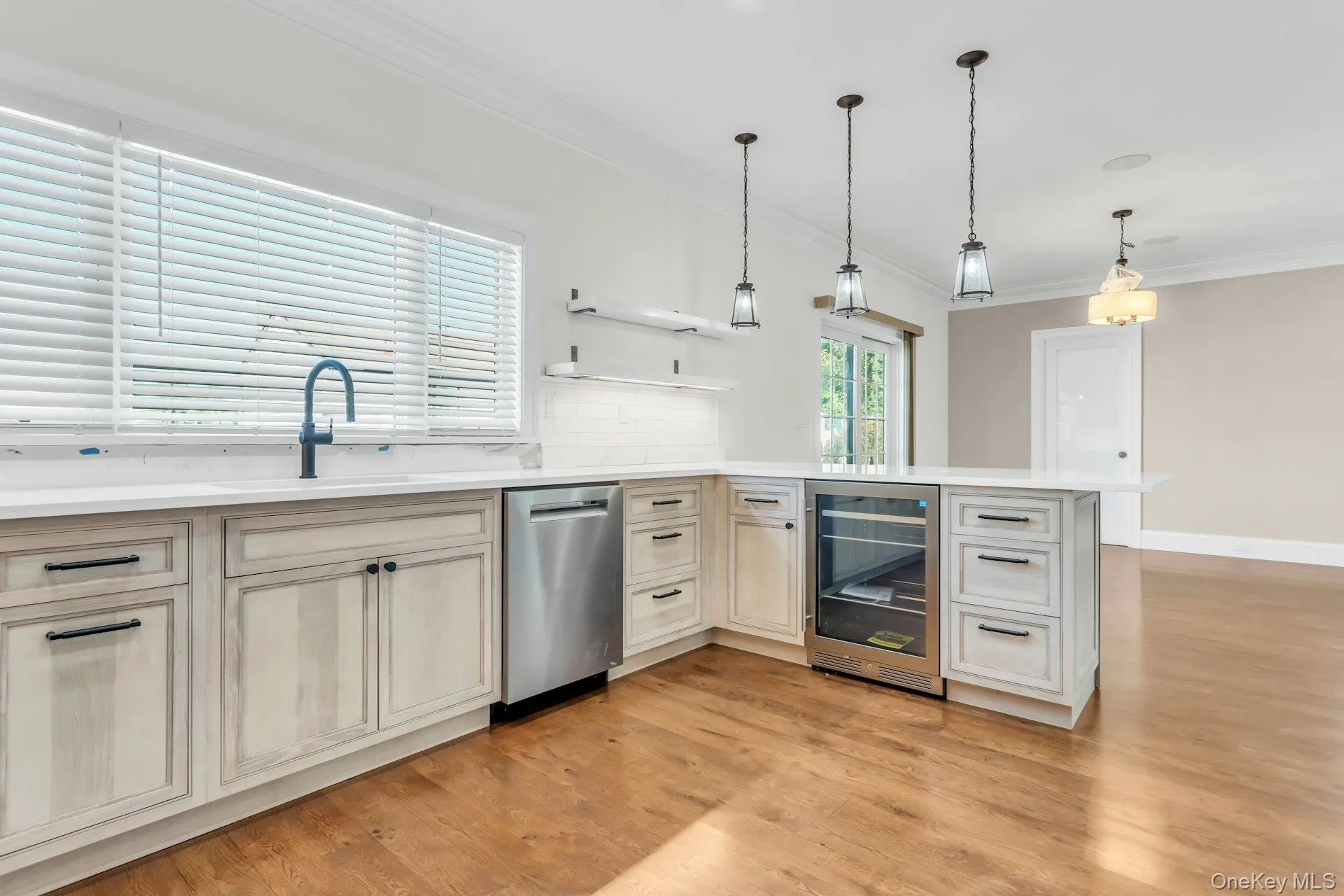 Kitchen featuring beverage cooler, a peninsula, crown molding, light wood-type flooring, and decorative backsplash Kitchen featuring beverage cooler, a peninsula, crown molding, light wood-type flooring, and decorative backsplash