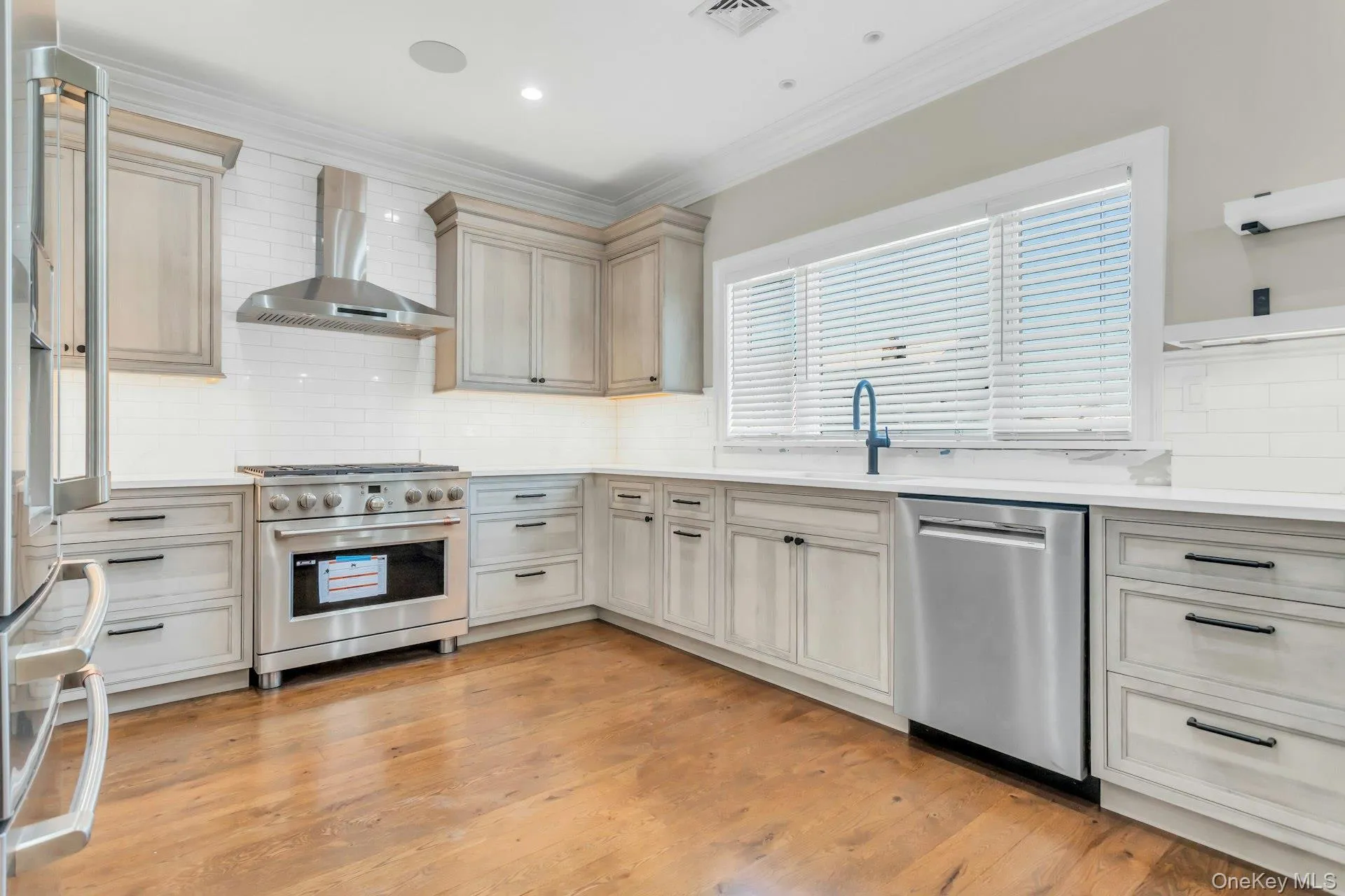 Kitchen featuring appliances with stainless steel finishes, wall chimney exhaust hood, backsplash, ornamental molding, and light stone counters Kitchen featuring appliances with stainless steel finishes, wall chimney exhaust hood, backsplash, ornamental molding, and light stone counters