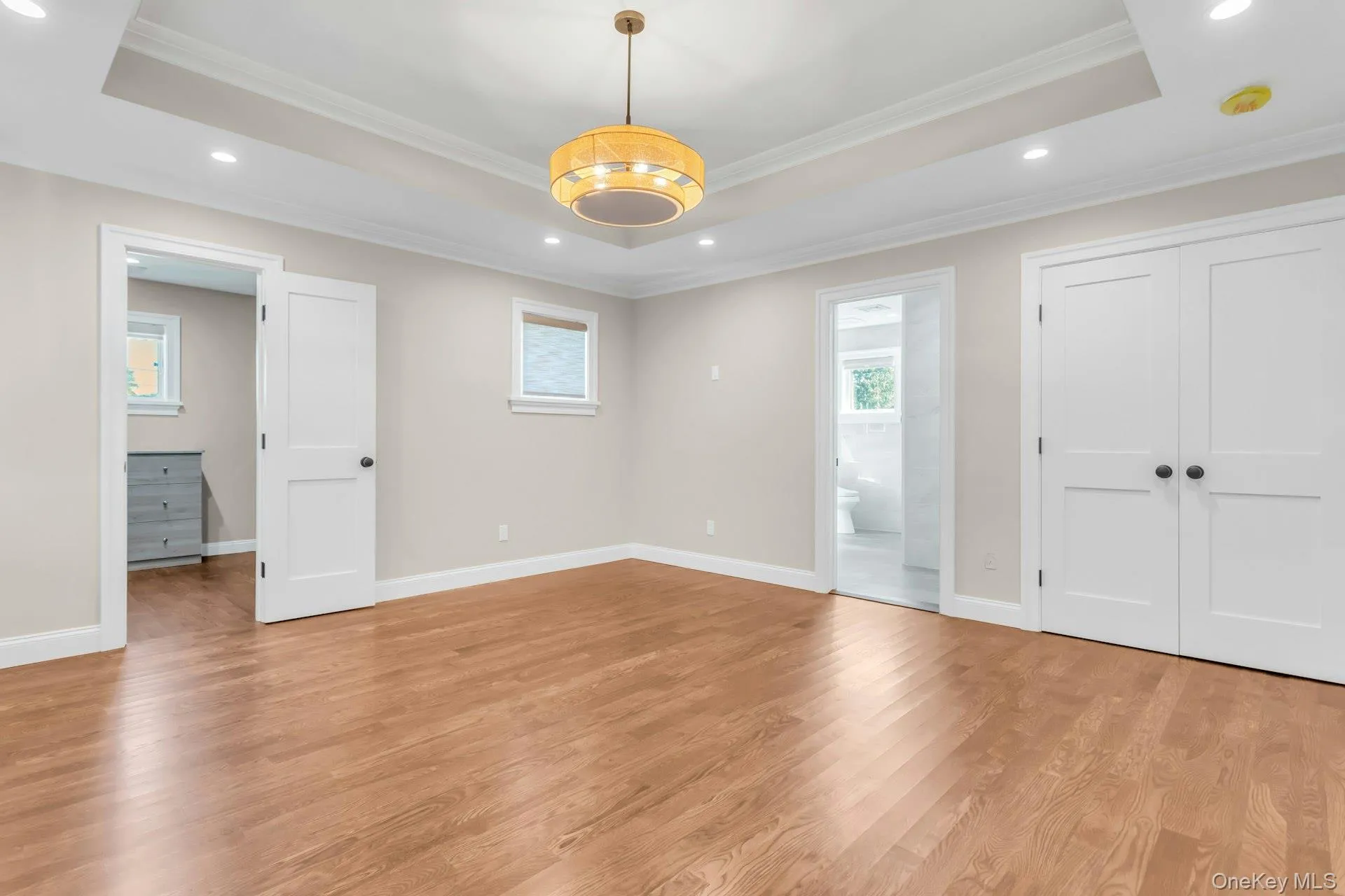 Unfurnished bedroom with a tray ceiling, recessed lighting, light wood finished floors, ornamental molding, and connected bathroom Unfurnished bedroom with a tray ceiling, recessed lighting, light wood finished floors, ornamental molding, and connected bathroom