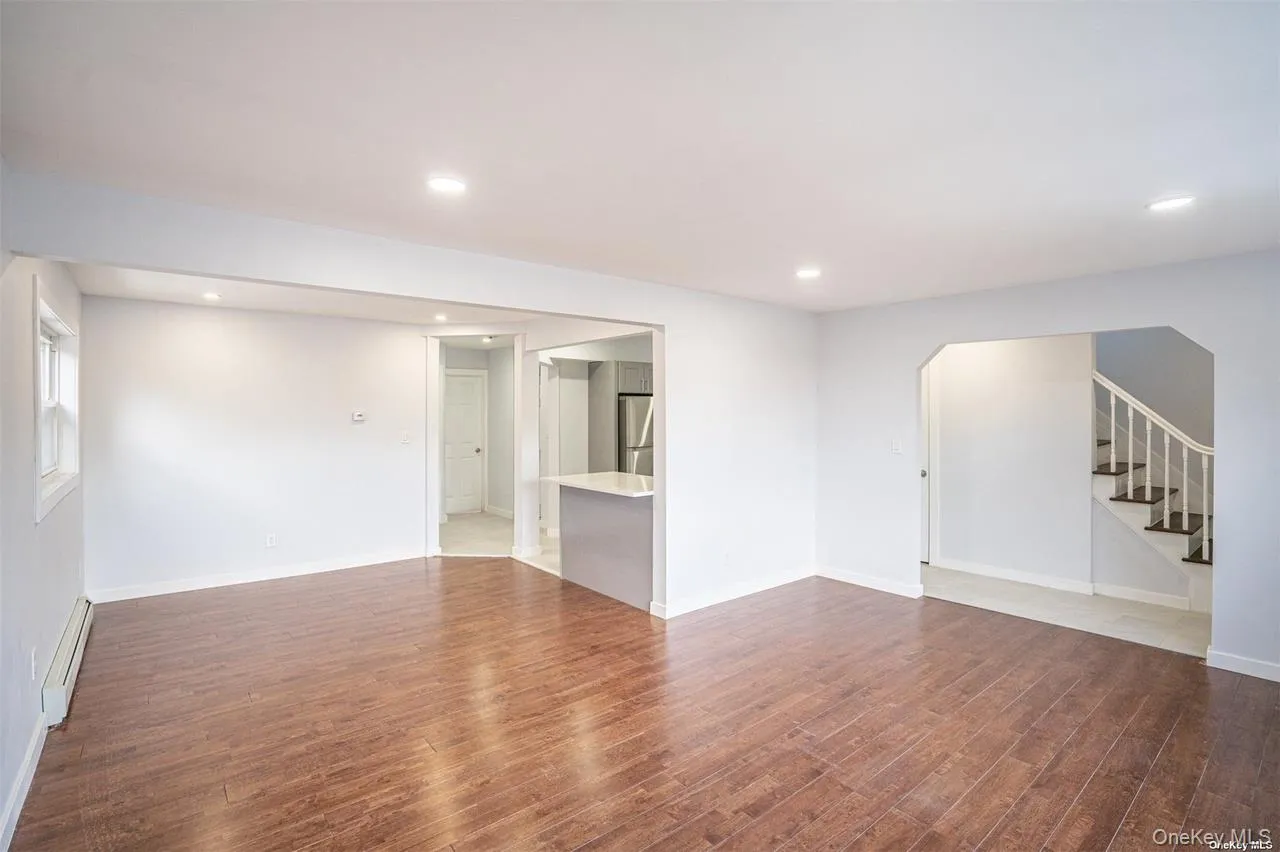 Unfurnished living room with dark wood finished floors, stairs, recessed lighting, baseboard heating, and arched walkways Unfurnished living room with dark wood finished floors, stairs, recessed lighting, baseboard heating, and arched walkways